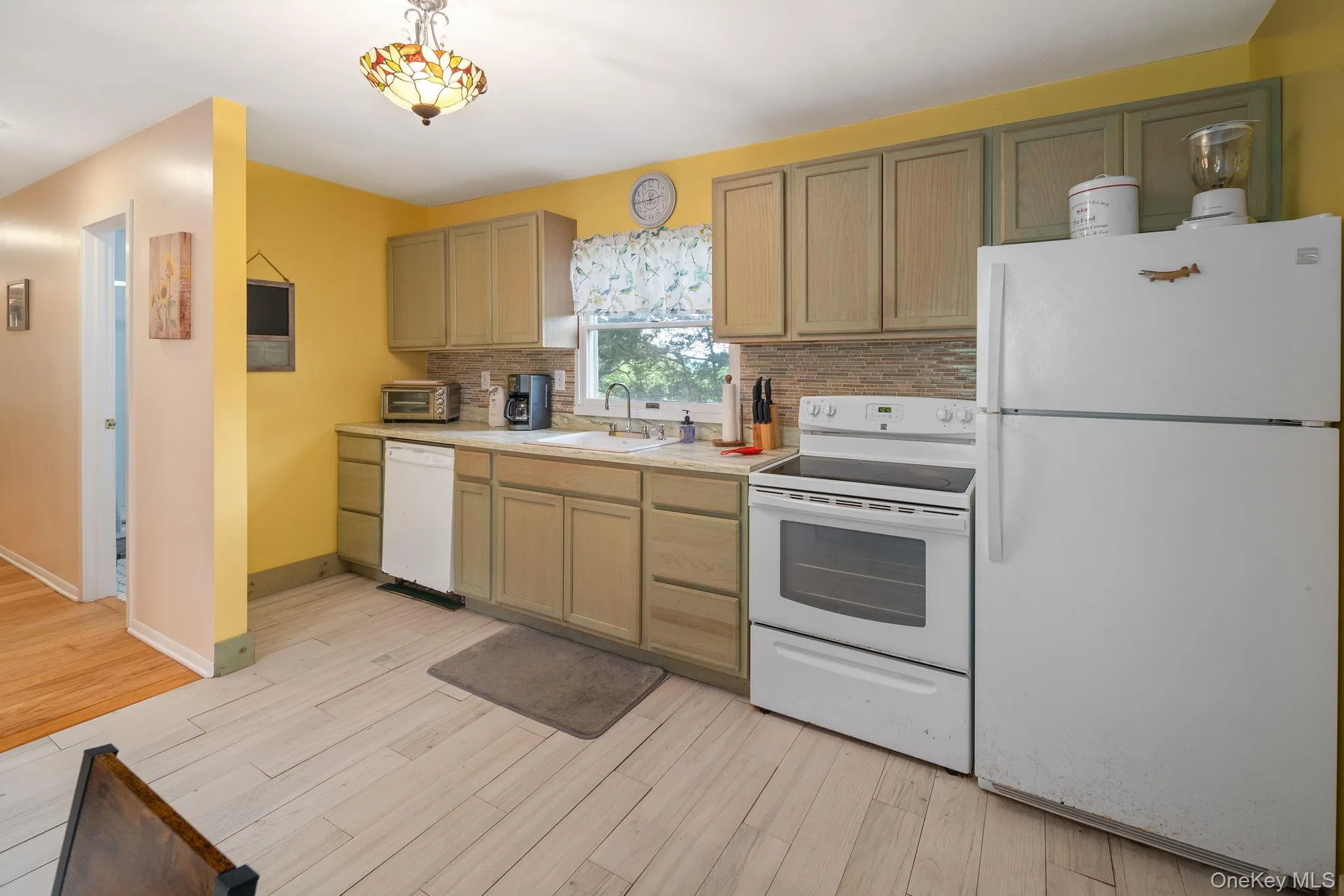Kitchen featuring wood-finish flooring, light-toned cabinetry, white appliances, and a tiled backsplash Kitchen featuring wood-finish flooring, light-toned cabinetry, white appliances, and a tiled backsplash