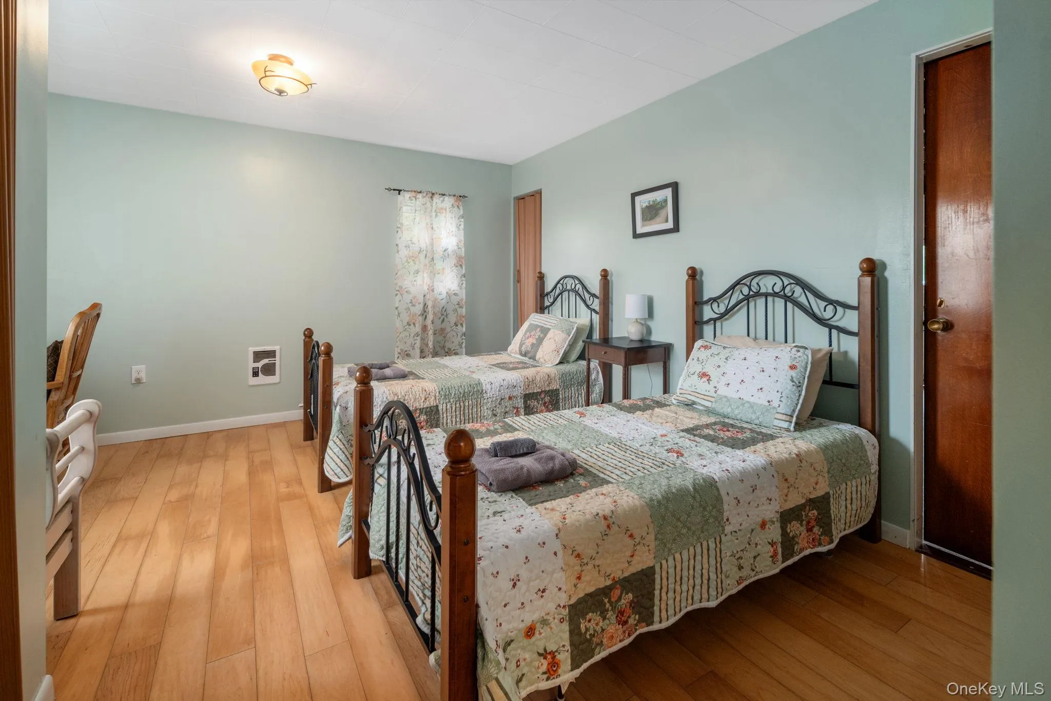 Wood-finish flooring, light green painted walls, window with sheer curtains, and a flush mount ceiling light fixture Wood-finish flooring, light green painted walls, window with sheer curtains, and a flush mount ceiling light fixture