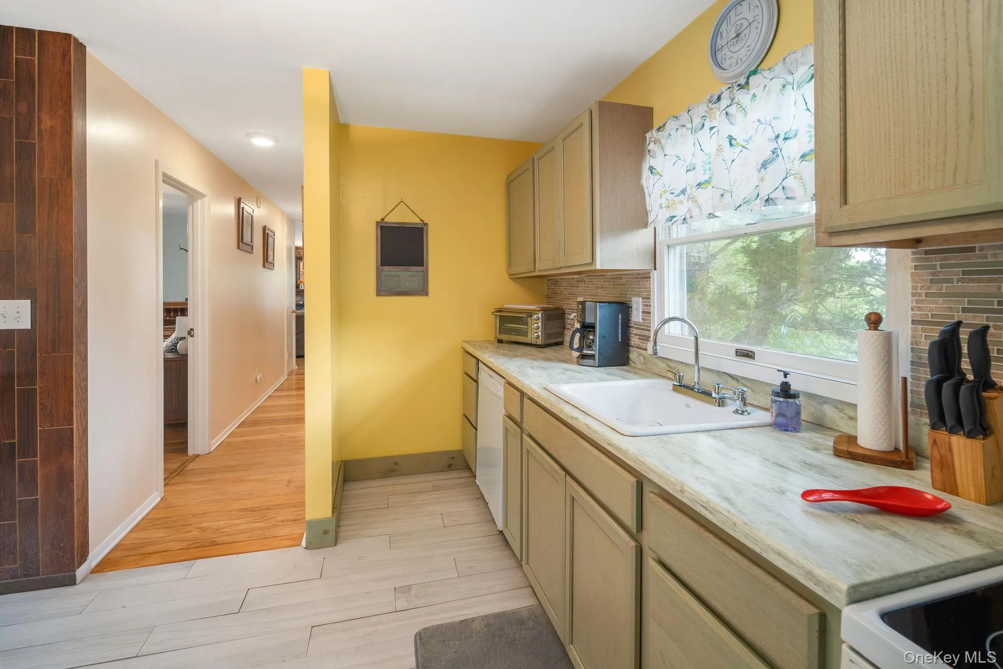 Built-in cabinetry with light-toned finishes, light-toned countertop, mosaic tile backsplash, and light wood-finish flooring in the hallway Built-in cabinetry with light-toned finishes, light-toned countertop, mosaic tile backsplash, and light wood-finish flooring in the hallway