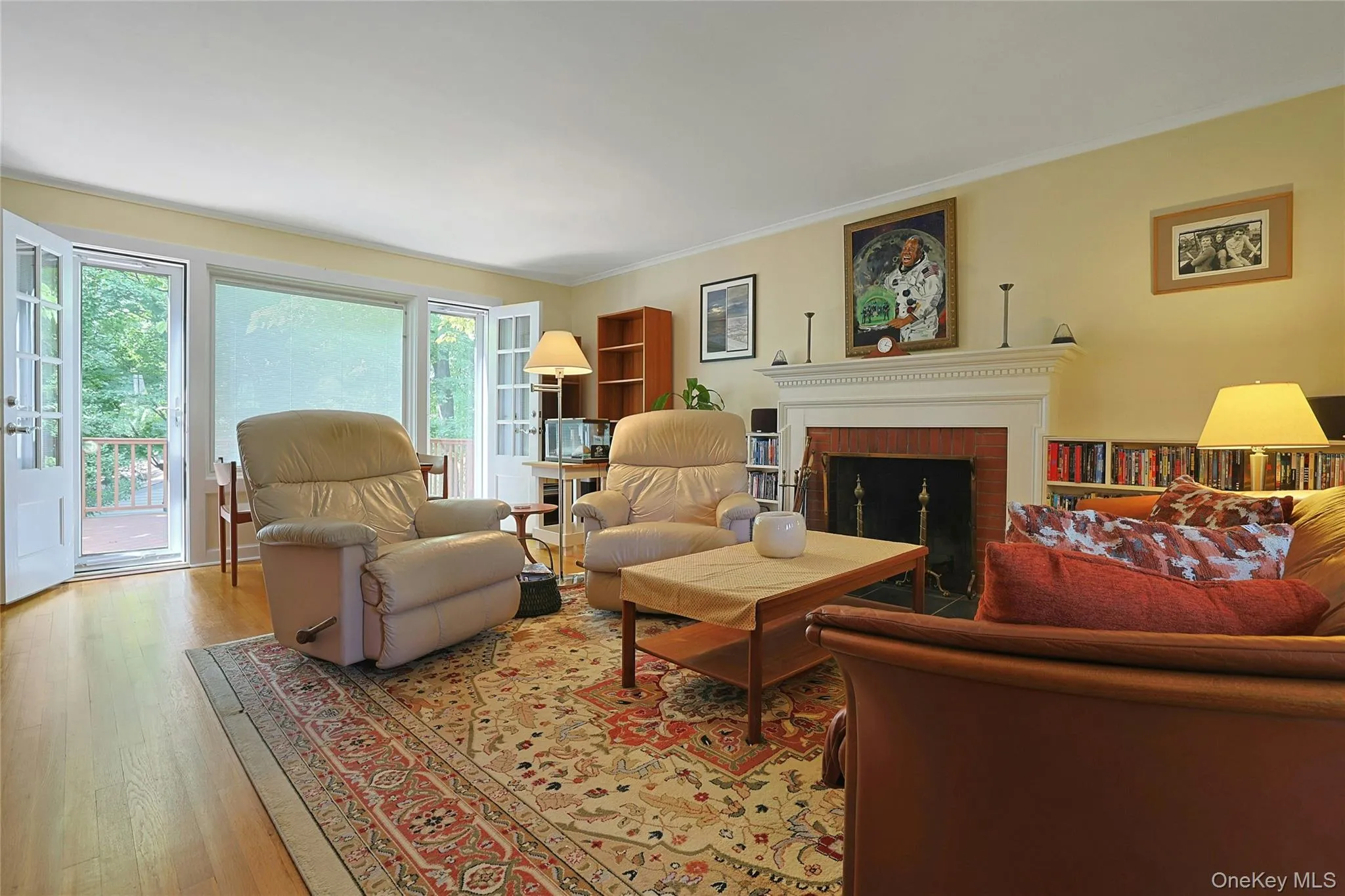 Another view showing the hardwood flooring, french doors leading to the deck, built-in shelving, white mantel, and a brick fireplace surround. Another view showing the hardwood flooring, french doors leading to the deck, built-in shelving, white mantel, and a brick fireplace surround.
