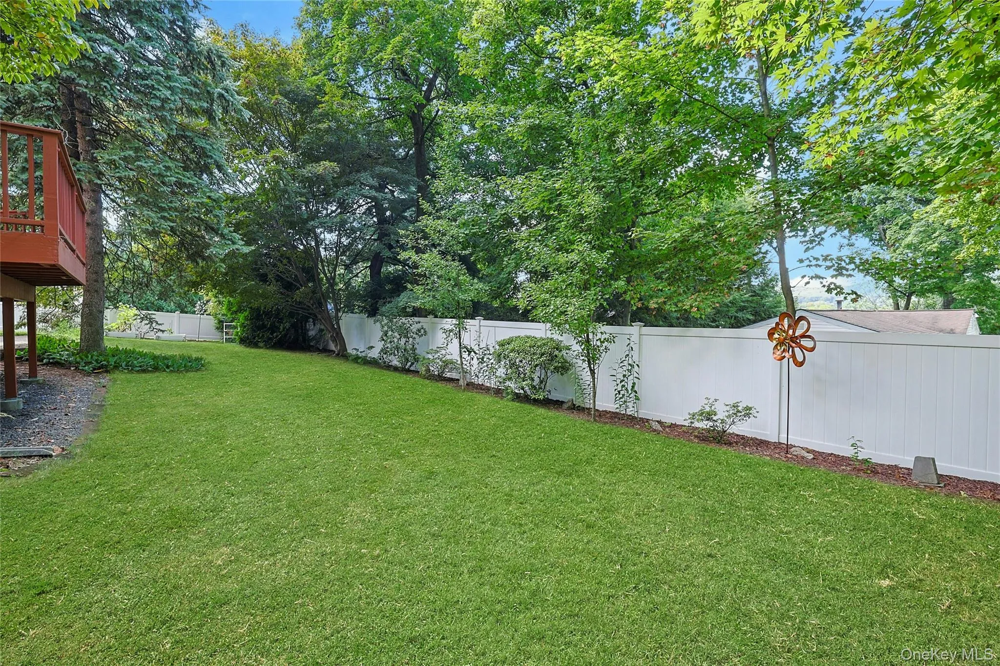 Another view of the expansive lawn area with a white privacy fence, mature trees, and a raised wooden deck. Another view of the expansive lawn area with a white privacy fence, mature trees, and a raised wooden deck.