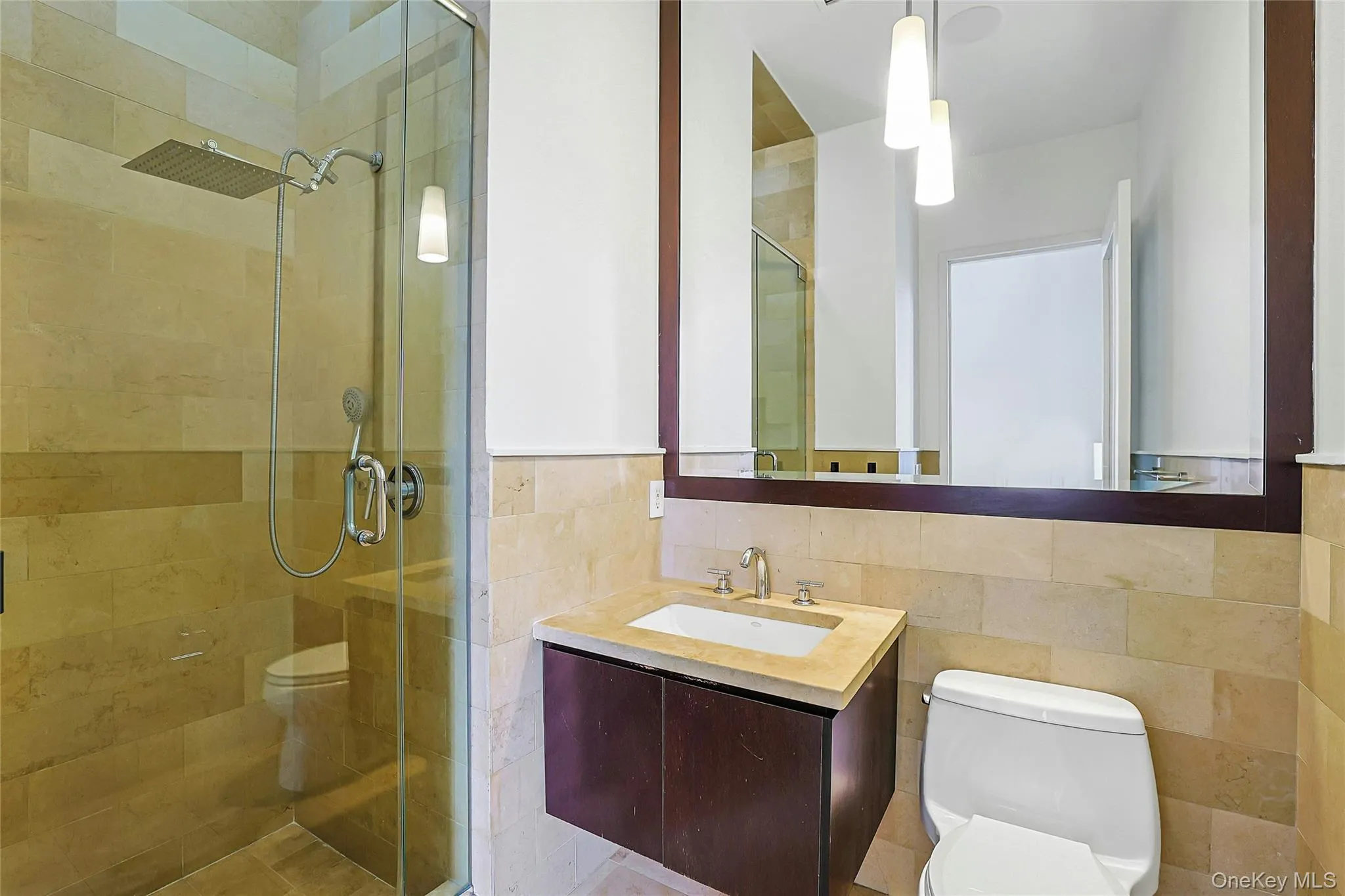 Tiled primary bathroom featuring a glass-enclosed shower, modern vanity, and large mirror. Tiled primary bathroom featuring a glass-enclosed shower, modern vanity, and large mirror.