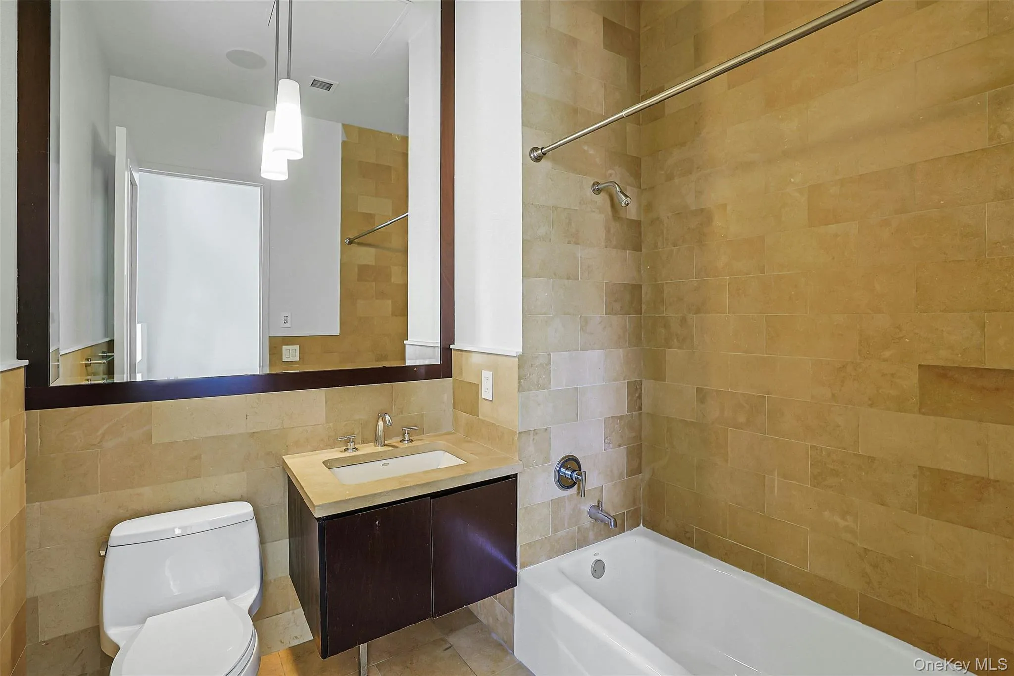 Full tiled bathroom featuring a tub/shower combination, modern vanity, and large mirror. Full tiled bathroom featuring a tub/shower combination, modern vanity, and large mirror.