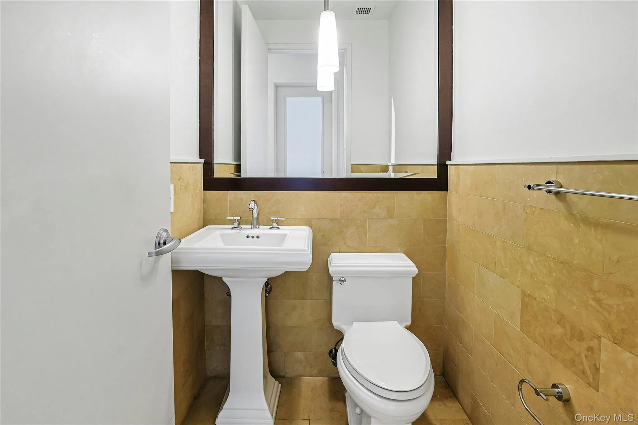 Convenient powder room featuring a pedestal sink, large mirror, and tiled walls. Convenient powder room featuring a pedestal sink, large mirror, and tiled walls.