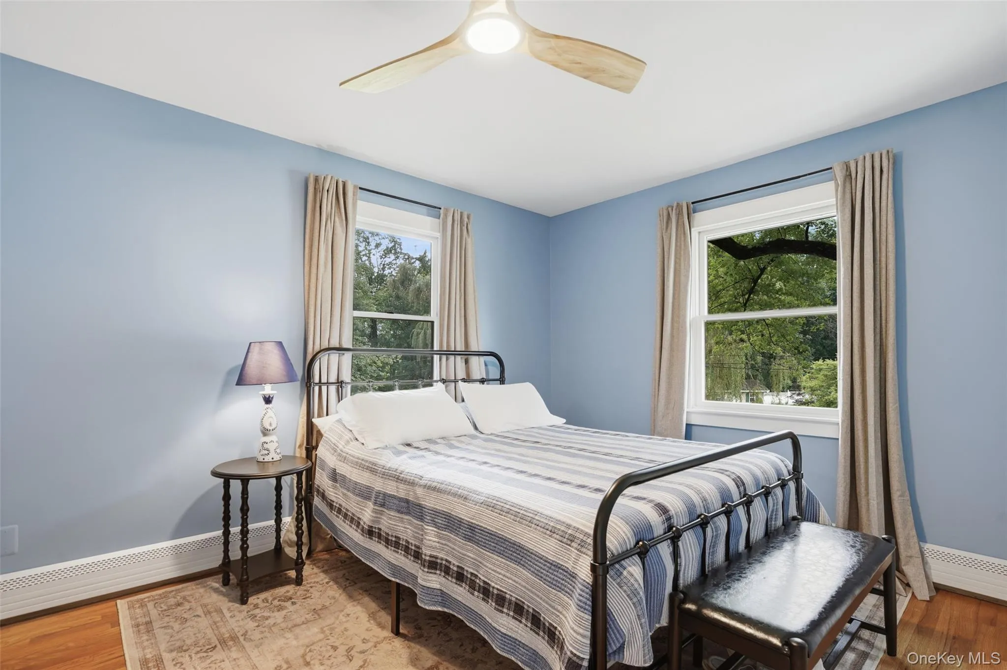 Hardwood flooring, two windows with drapery, and a ceiling fan with light fixture Hardwood flooring, two windows with drapery, and a ceiling fan with light fixture
