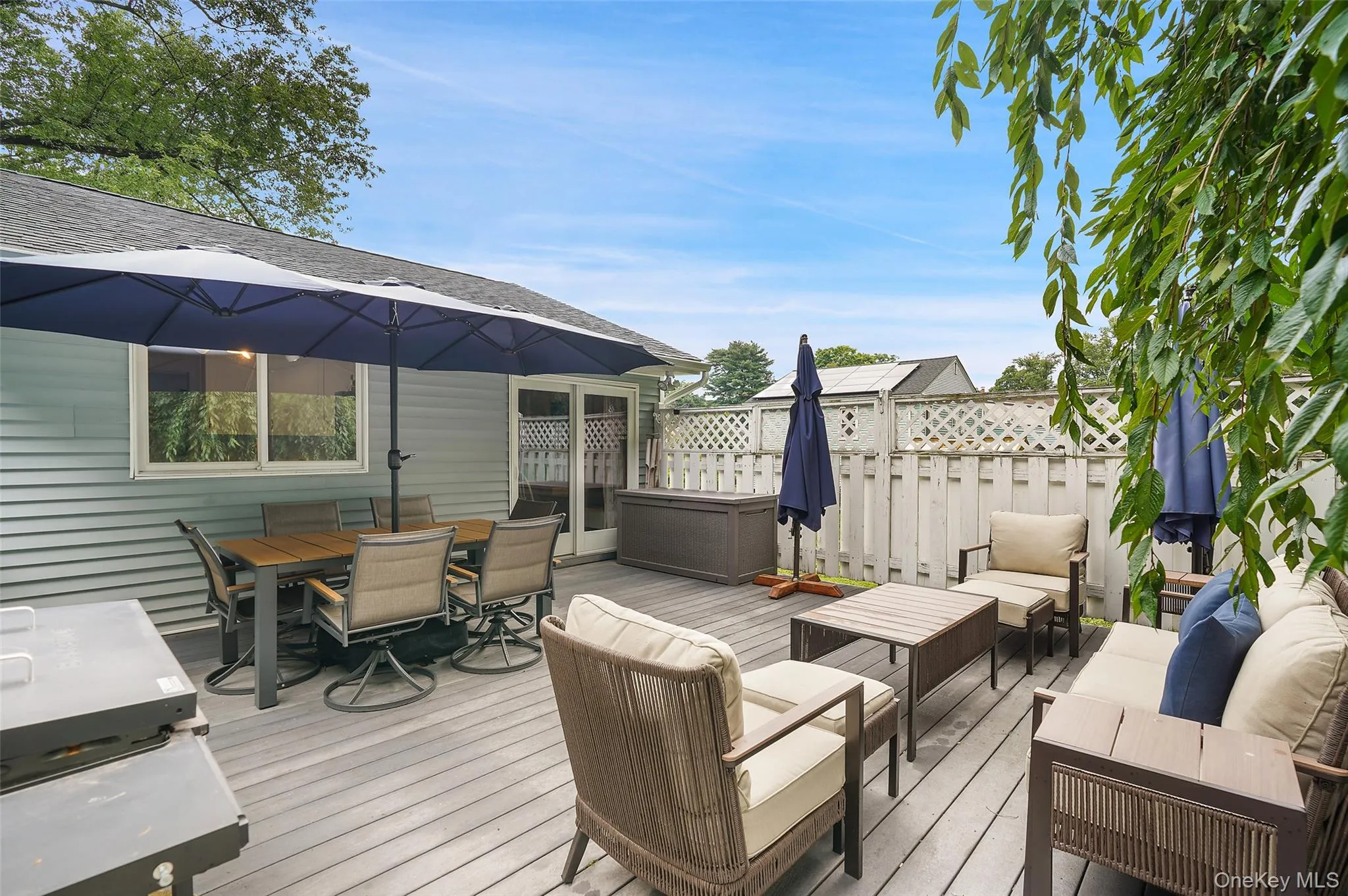 Expansive wood-finish deck with multiple seating areas, a sliding glass door, and privacy fencing Expansive wood-finish deck with multiple seating areas, a sliding glass door, and privacy fencing