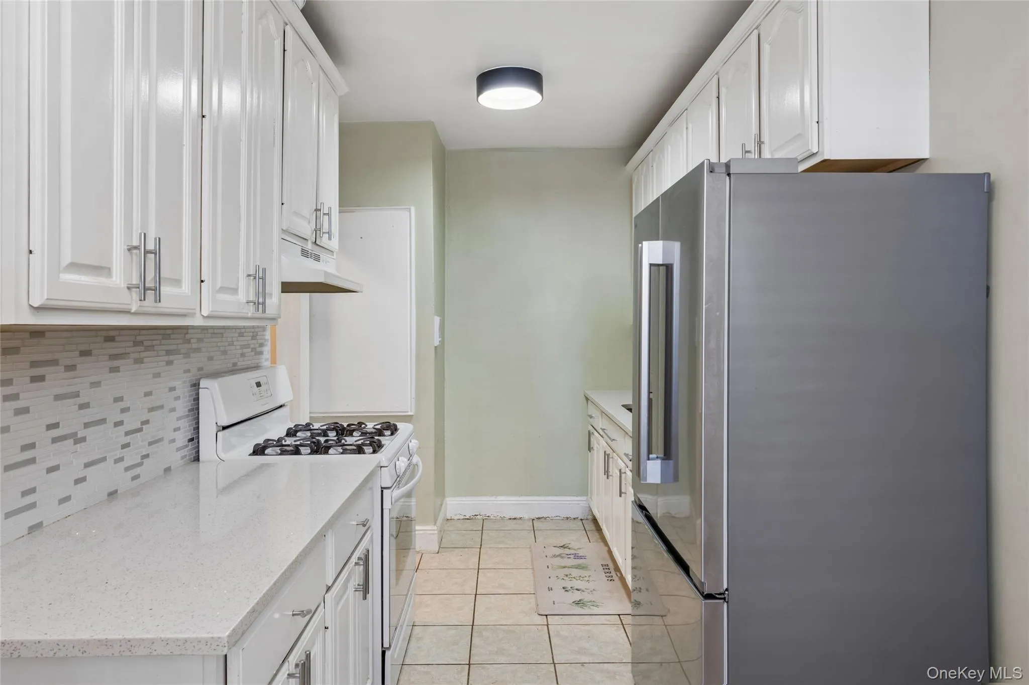 White cabinetry with brushed nickel hardware, light-toned countertops, mosaic tile backsplash, and tile flooring White cabinetry with brushed nickel hardware, light-toned countertops, mosaic tile backsplash, and tile flooring