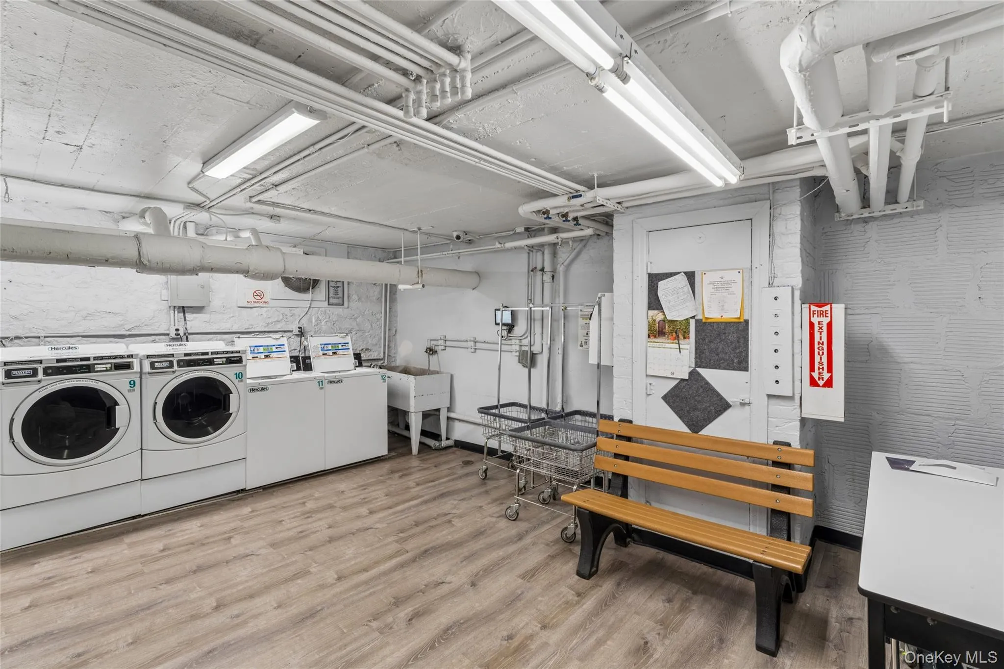 Wood-finish flooring with multiple washers and dryers, a utility sink, and overhead fluorescent lighting Wood-finish flooring with multiple washers and dryers, a utility sink, and overhead fluorescent lighting