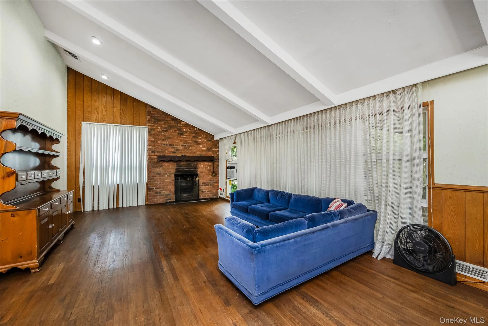 Vaulted ceiling with exposed beams, brick fireplace, wood-finish flooring, wood panel accent walls, and recessed lighting Vaulted ceiling with exposed beams, brick fireplace, wood-finish flooring, wood panel accent walls, and recessed lighting