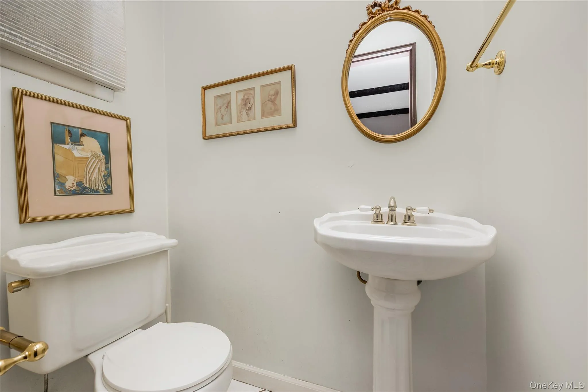 Half bath on main floor with pedestal sink, polished nickel faucet, white toilet with brass flush lever, and decorative oval mirror Half bath on main floor with pedestal sink, polished nickel faucet, white toilet with brass flush lever, and decorative oval mirror