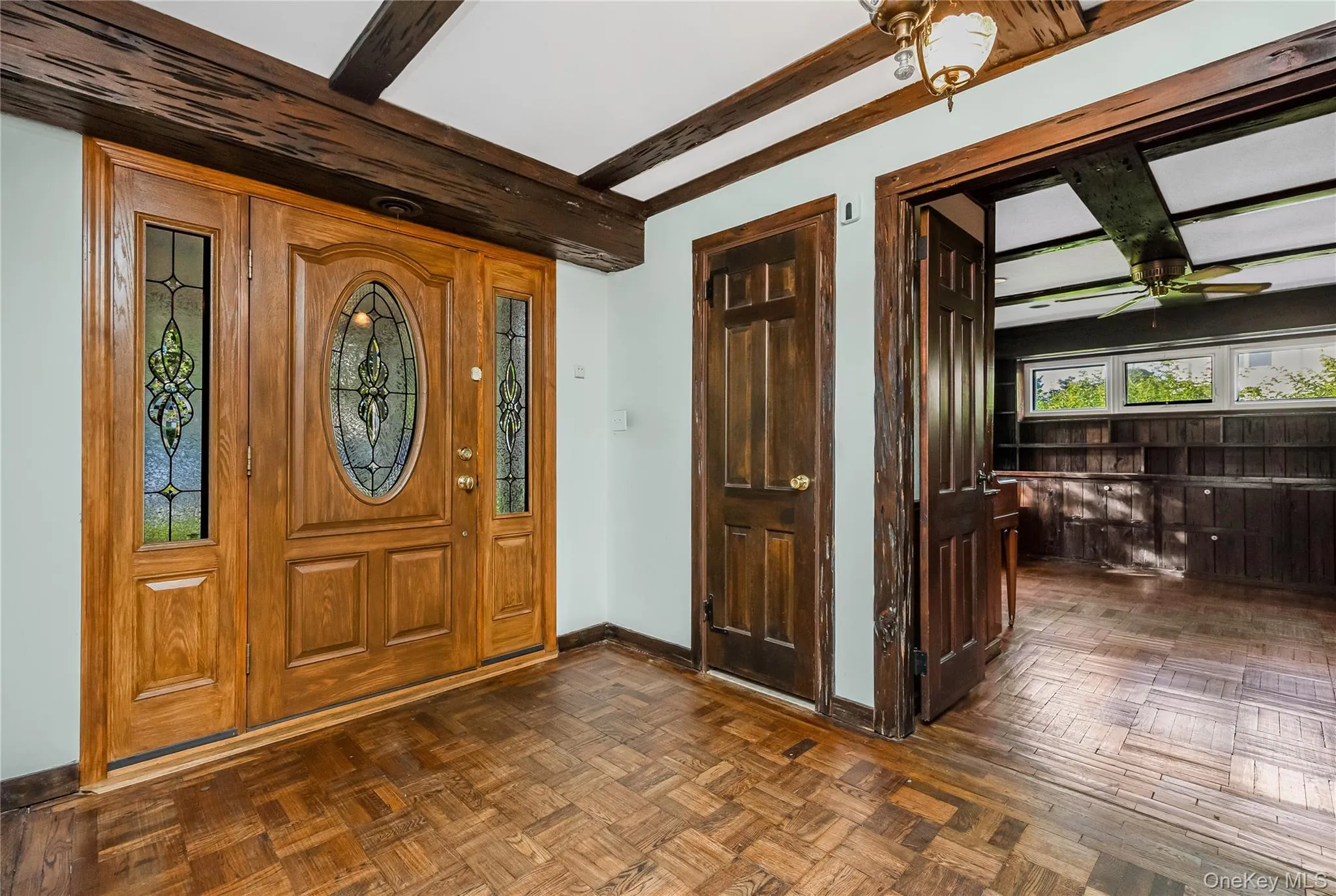 Entrance with leaded glass door and sidelights, exposed wood beams, and parquet flooring Entrance with leaded glass door and sidelights, exposed wood beams, and parquet flooring