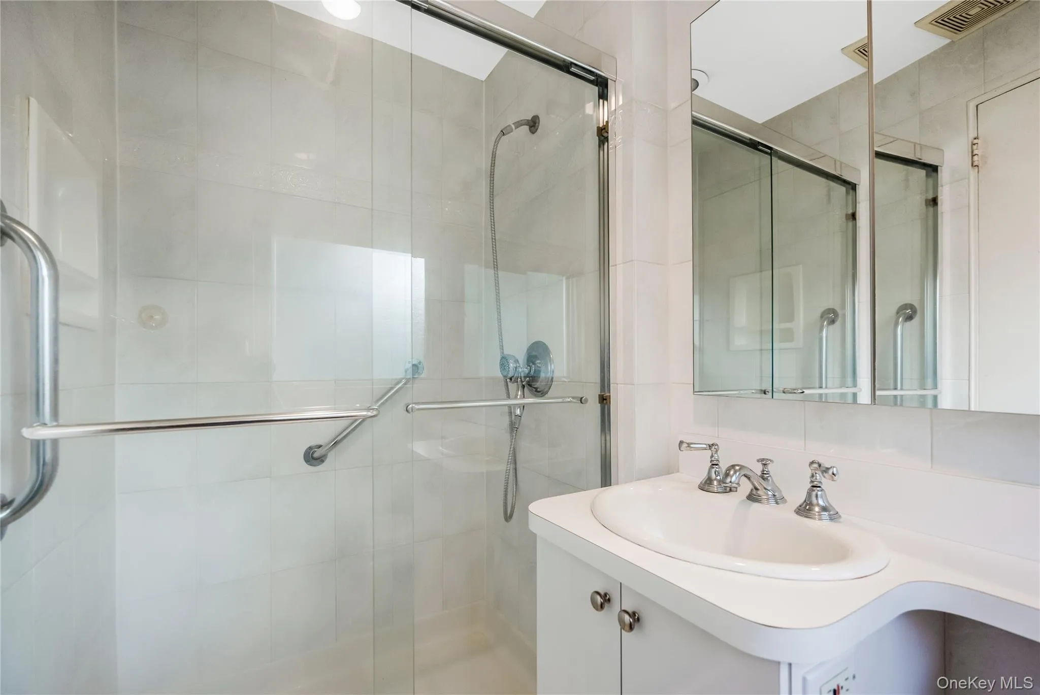 Glass-enclosed shower with ceramic tile surround, chrome fixtures, built-in medicine cabinet, and a vanity with a drop-in sink Glass-enclosed shower with ceramic tile surround, chrome fixtures, built-in medicine cabinet, and a vanity with a drop-in sink
