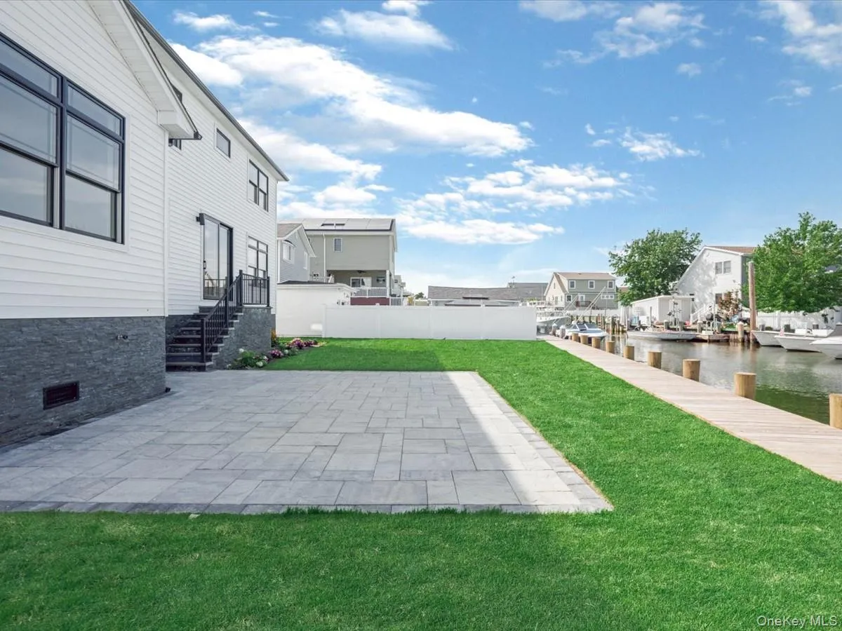 Spacious backyard featuring a stone paver patio, lush green lawn, and a private wooden dock leading to the canal Spacious backyard featuring a stone paver patio, lush green lawn, and a private wooden dock leading to the canal