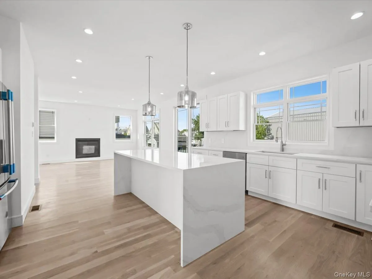 Spacious kitchen featuring an expansive island, white cabinetry, integrated stainless steel appliances, and wood-finish flooring Spacious kitchen featuring an expansive island, white cabinetry, integrated stainless steel appliances, and wood-finish flooring