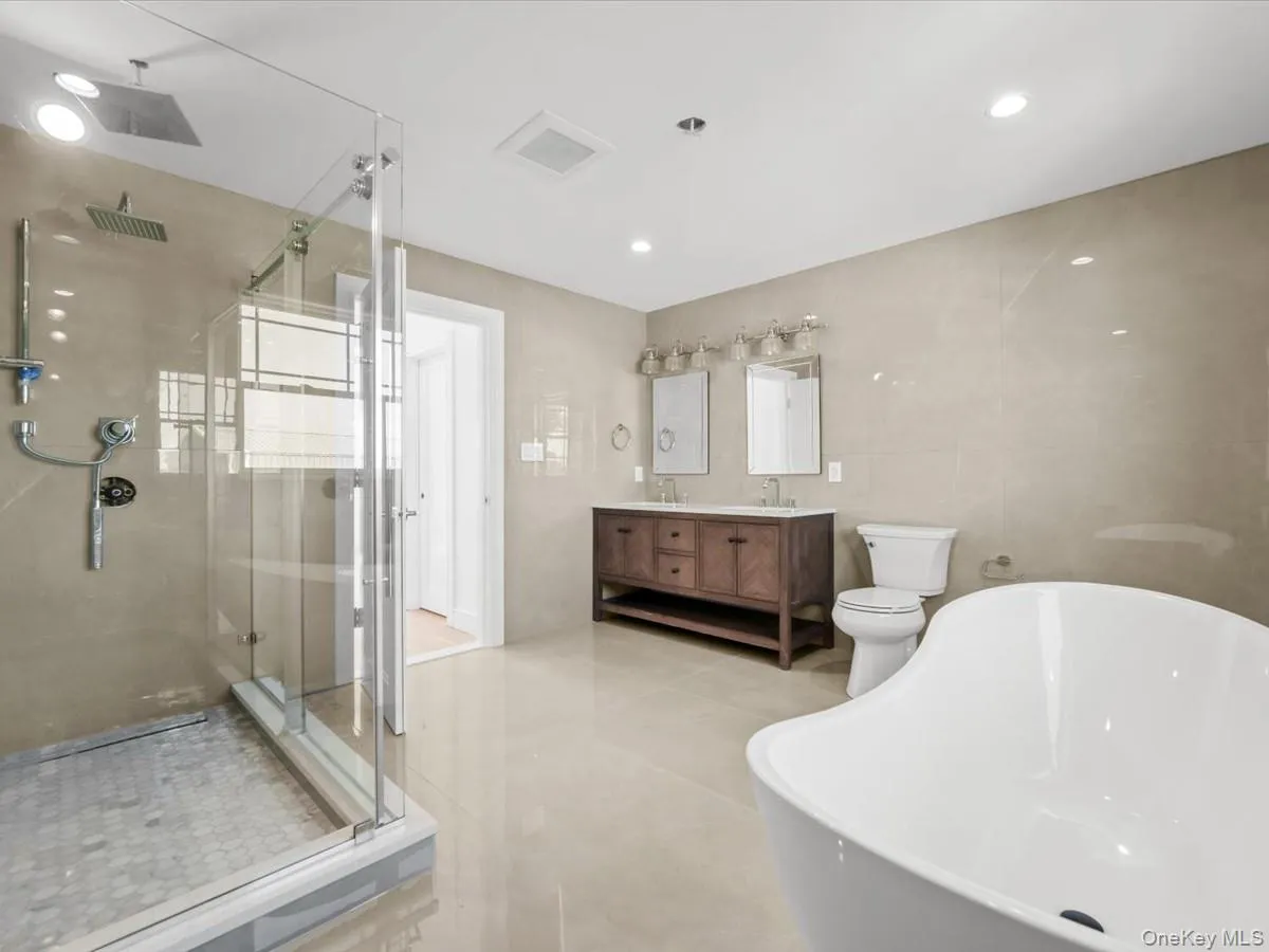 Spacious bathroom featuring a freestanding soaking tub, glass-enclosed shower with rain head, dual vanity with undermount sinks, and light-toned tile flooring Spacious bathroom featuring a freestanding soaking tub, glass-enclosed shower with rain head, dual vanity with undermount sinks, and light-toned tile flooring