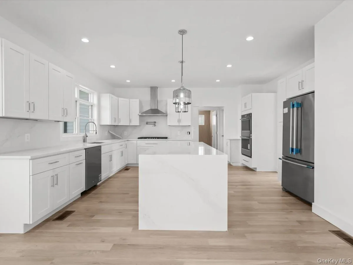 Kitchen featuring an expansive center island, integrated stainless steel appliances, recessed lighting, and wood-finish flooring Kitchen featuring an expansive center island, integrated stainless steel appliances, recessed lighting, and wood-finish flooring