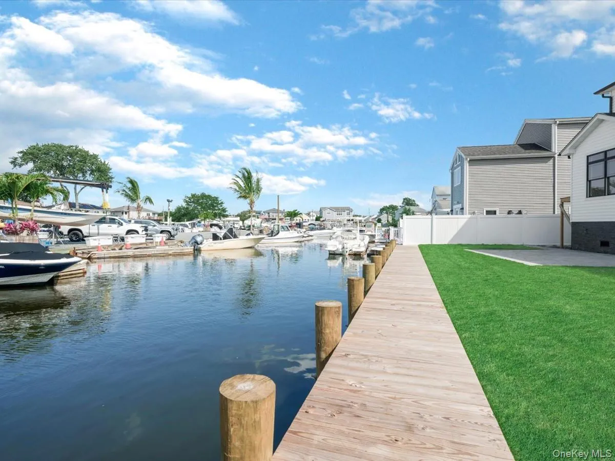 Waterside wooden dock with multiple boat slips, flanked by a manicured green lawn and a privacy fence Waterside wooden dock with multiple boat slips, flanked by a manicured green lawn and a privacy fence