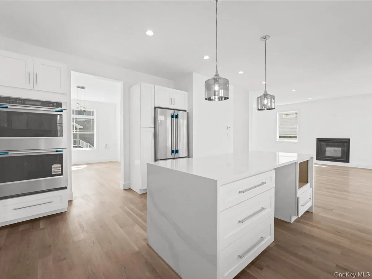 Kitchen featuring a white center island, stainless steel double oven, stainless steel refrigerator, white cabinetry, and wood-finish flooring Kitchen featuring a white center island, stainless steel double oven, stainless steel refrigerator, white cabinetry, and wood-finish flooring