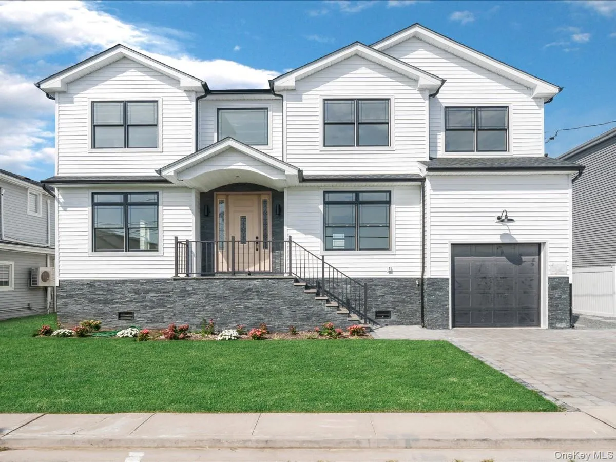 White siding exterior featuring a multi-gable roofline, black-framed windows, a light wood-finish entry door, and dark stone-clad foundation White siding exterior featuring a multi-gable roofline, black-framed windows, a light wood-finish entry door, and dark stone-clad foundation