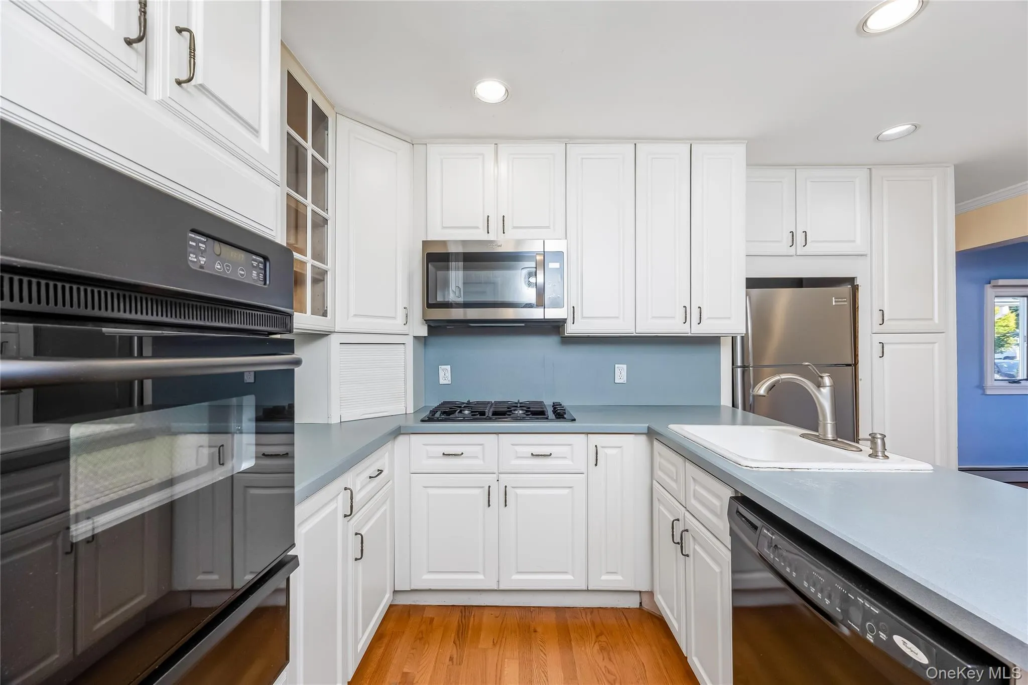 EIK with white cabinetry, wood-finish flooring, stainless steel appliances, built-in oven, and a gas cooktop EIK with white cabinetry, wood-finish flooring, stainless steel appliances, built-in oven, and a gas cooktop