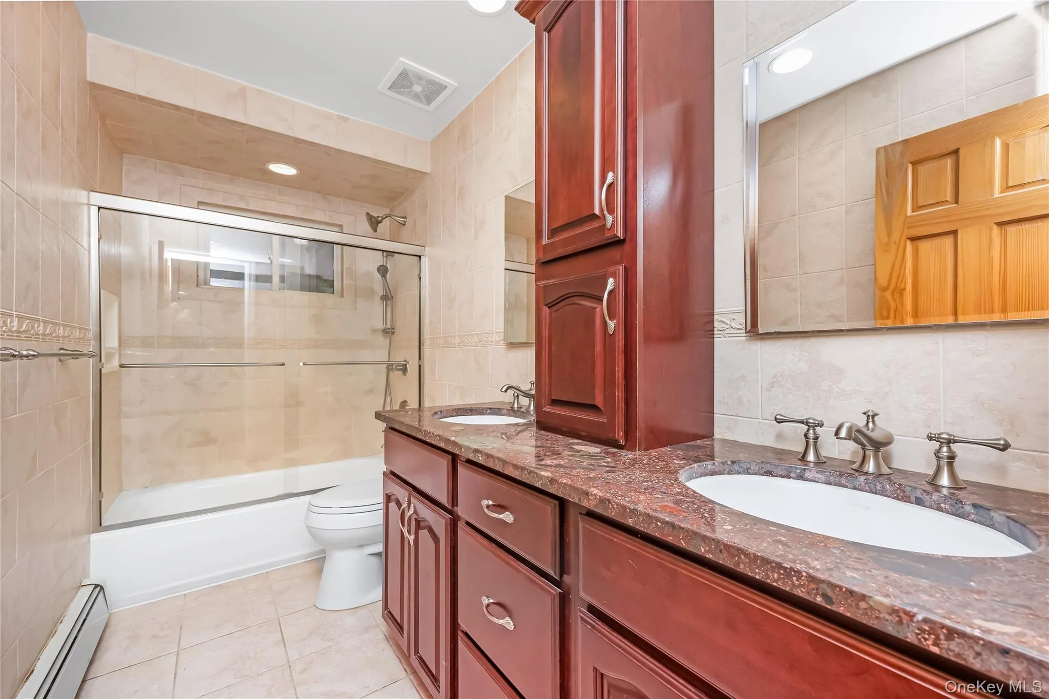 Hall bathroom featuring a dual-sink vanity with rich wood cabinetry, granite countertop, and polished nickel fixtures Hall bathroom featuring a dual-sink vanity with rich wood cabinetry, granite countertop, and polished nickel fixtures