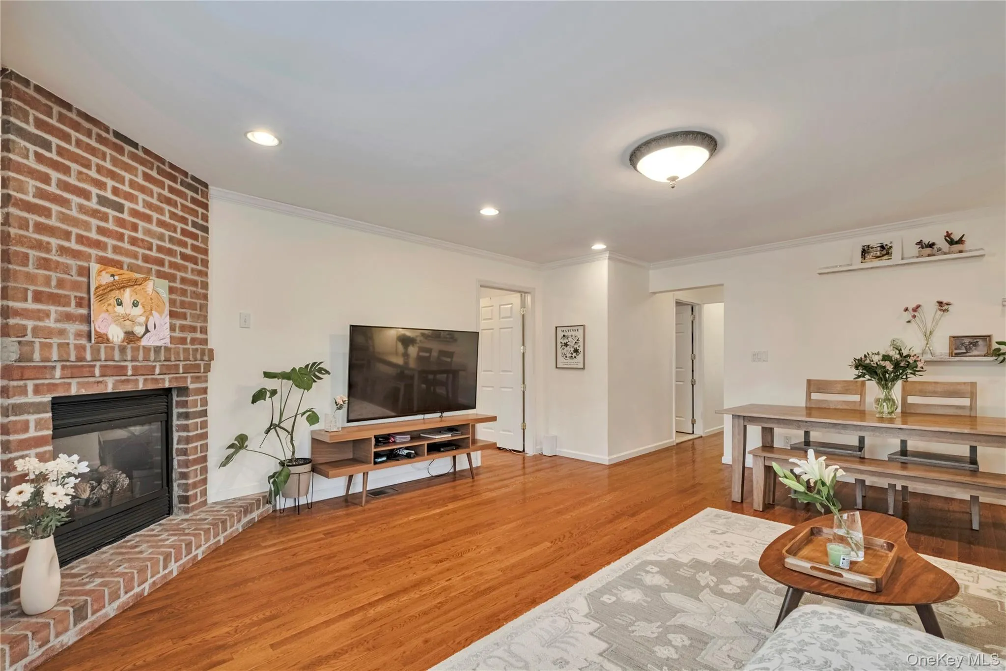 Living area featuring crown molding, wood finished floors, a brick fireplace, and recessed lighting Living area featuring crown molding, wood finished floors, a brick fireplace, and recessed lighting