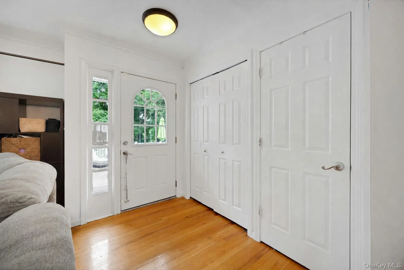 Entryway featuring wood-finish flooring, a white paneled door with an arched window, a sidelight, and two white bi-fold closet doors Entryway featuring wood-finish flooring, a white paneled door with an arched window, a sidelight, and two white bi-fold closet doors