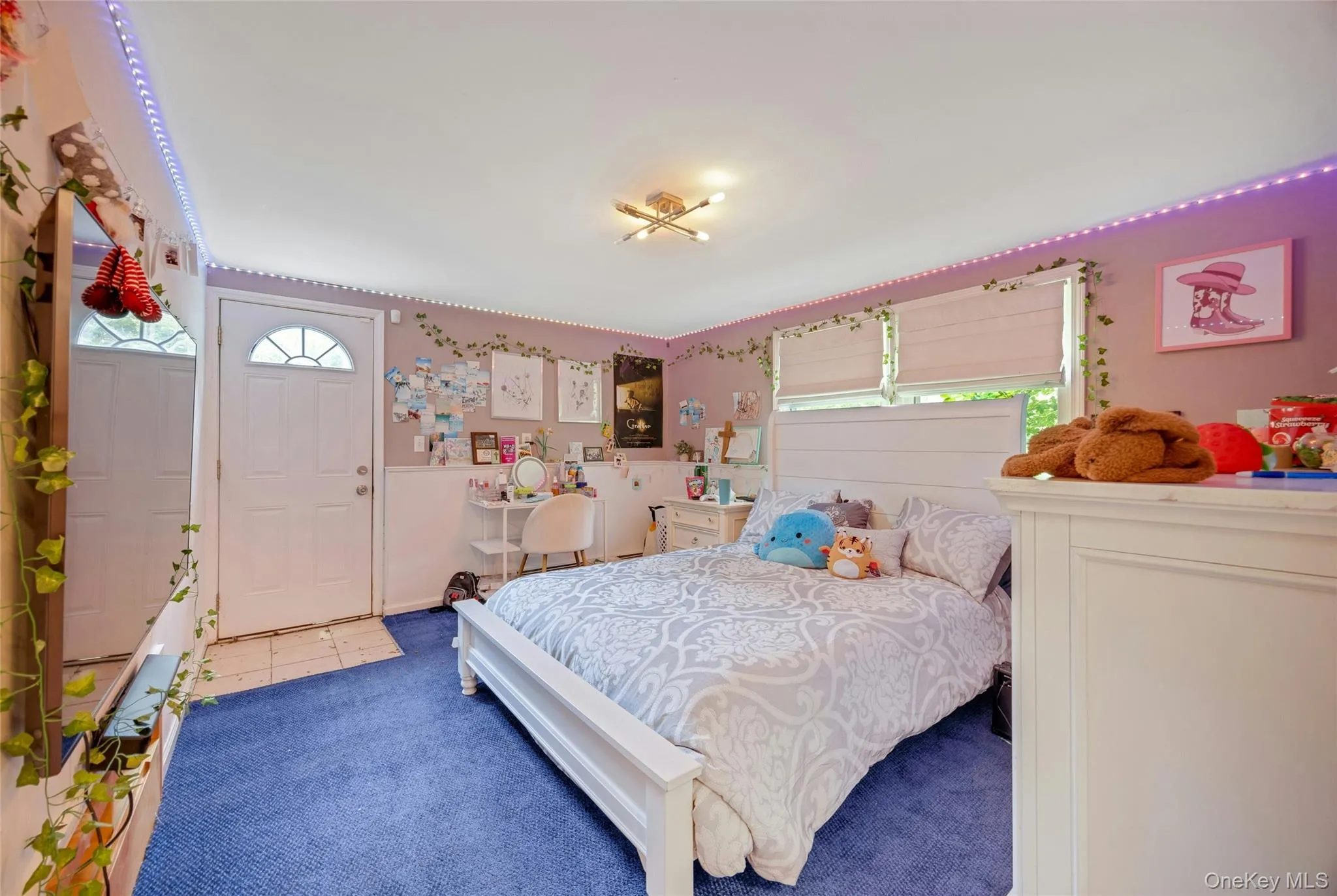 Room featuring a white paneled door with a sunburst window, two windows with blinds, and blue carpeting Room featuring a white paneled door with a sunburst window, two windows with blinds, and blue carpeting