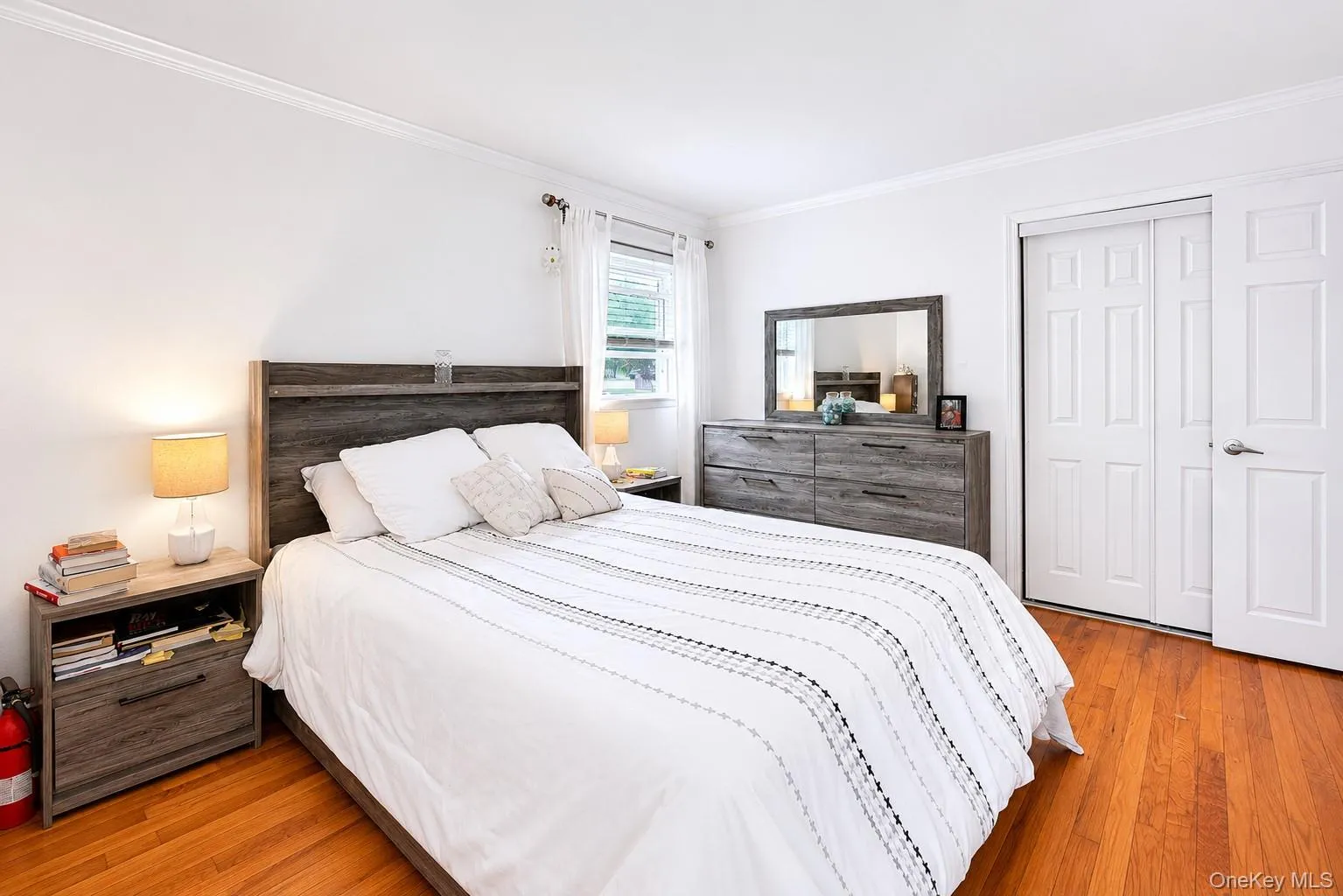 Spacious bedroom featuring wood-finish flooring, white walls, and crown molding Spacious bedroom featuring wood-finish flooring, white walls, and crown molding