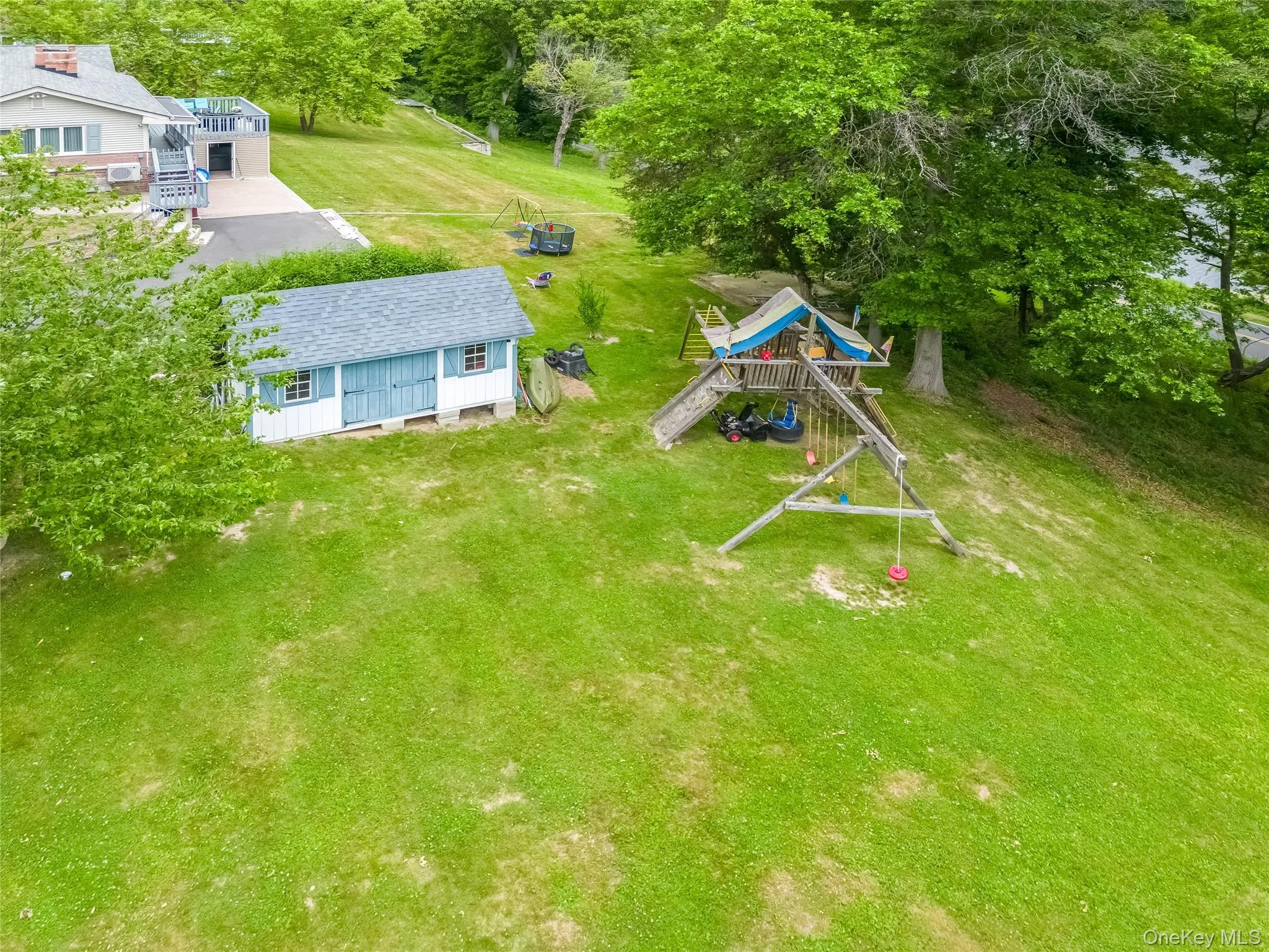 Expansive green lawn featuring a detached shed with light blue double doors and a wood playset under mature trees Expansive green lawn featuring a detached shed with light blue double doors and a wood playset under mature trees