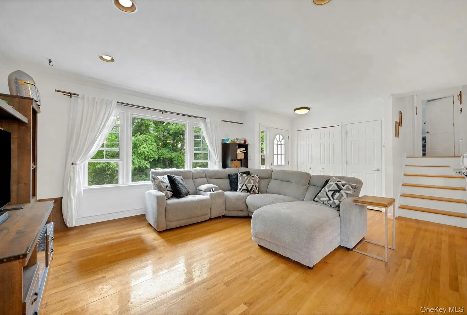 Bright living area featuring wood-finish flooring, recessed lighting, and a multi-pane window overlooking mature trees Bright living area featuring wood-finish flooring, recessed lighting, and a multi-pane window overlooking mature trees