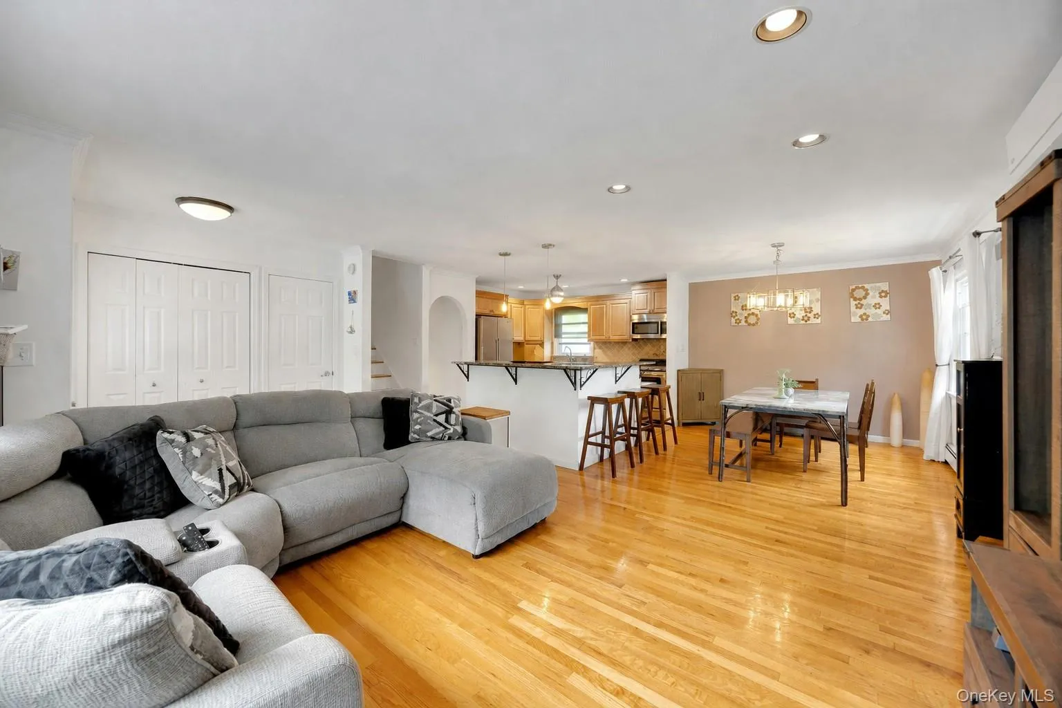 Bright open-concept living space featuring wood-finish flooring, recessed lighting, and a kitchen island with seating Bright open-concept living space featuring wood-finish flooring, recessed lighting, and a kitchen island with seating