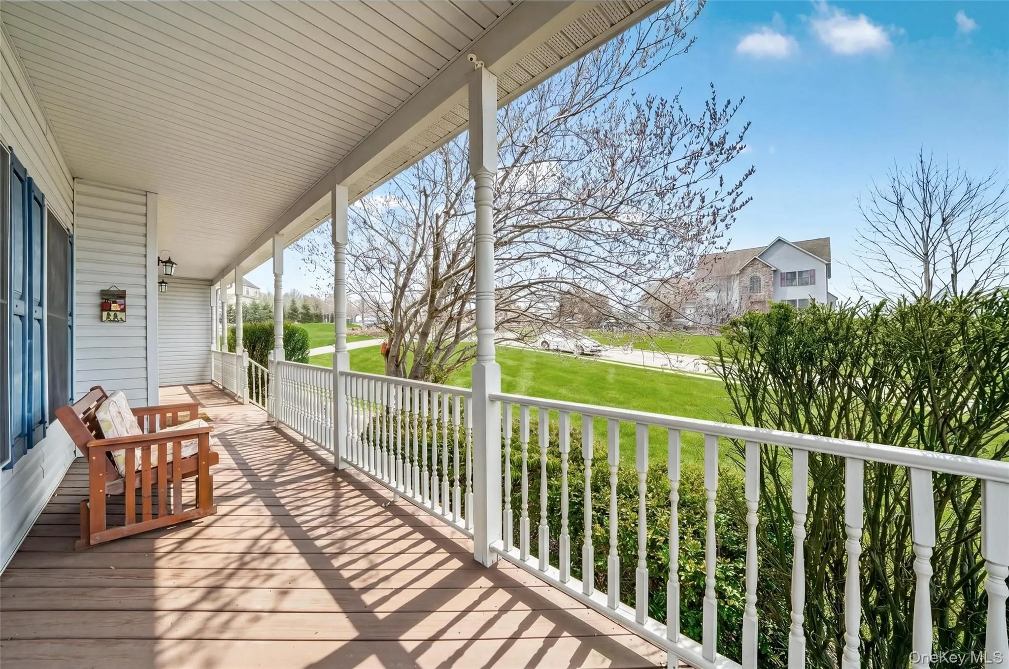 Expansive covered front porch featuring wood-finish flooring, white spindle railings, and decorative columns Expansive covered front porch featuring wood-finish flooring, white spindle railings, and decorative columns