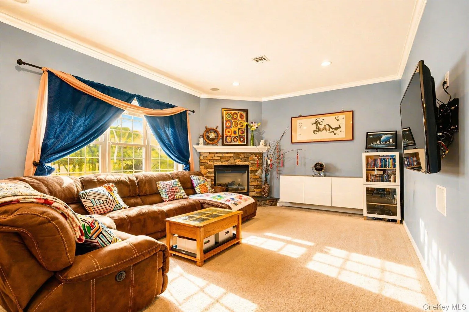 Living area featuring a stone-clad fireplace, large multi-pane windows, recessed lighting, crown molding, and a wall-mounted television bracket Living area featuring a stone-clad fireplace, large multi-pane windows, recessed lighting, crown molding, and a wall-mounted television bracket