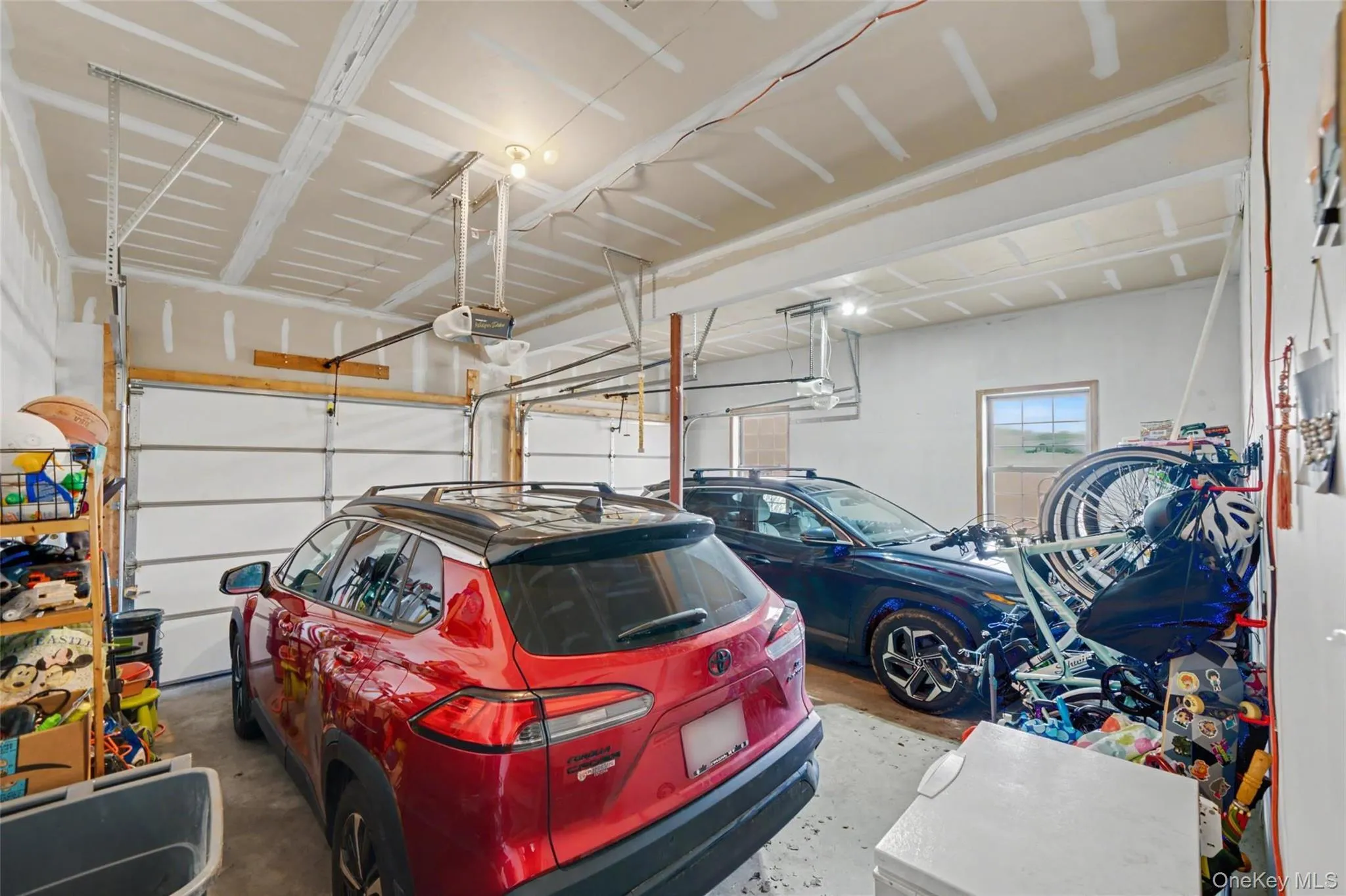 Two-car garage featuring segmented overhead doors, exposed ceiling joists, and a rear window Two-car garage featuring segmented overhead doors, exposed ceiling joists, and a rear window