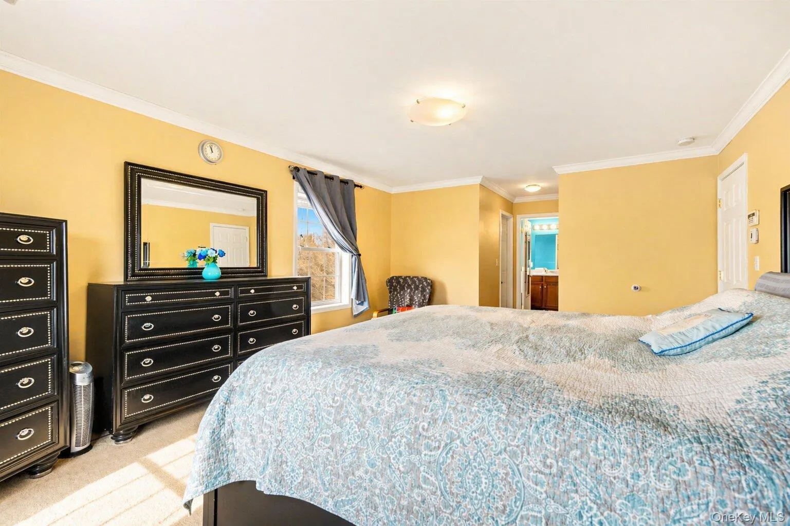 Carpeted bedroom featuring a window with curtain, crown molding, and a flush mount ceiling light fixture Carpeted bedroom featuring a window with curtain, crown molding, and a flush mount ceiling light fixture