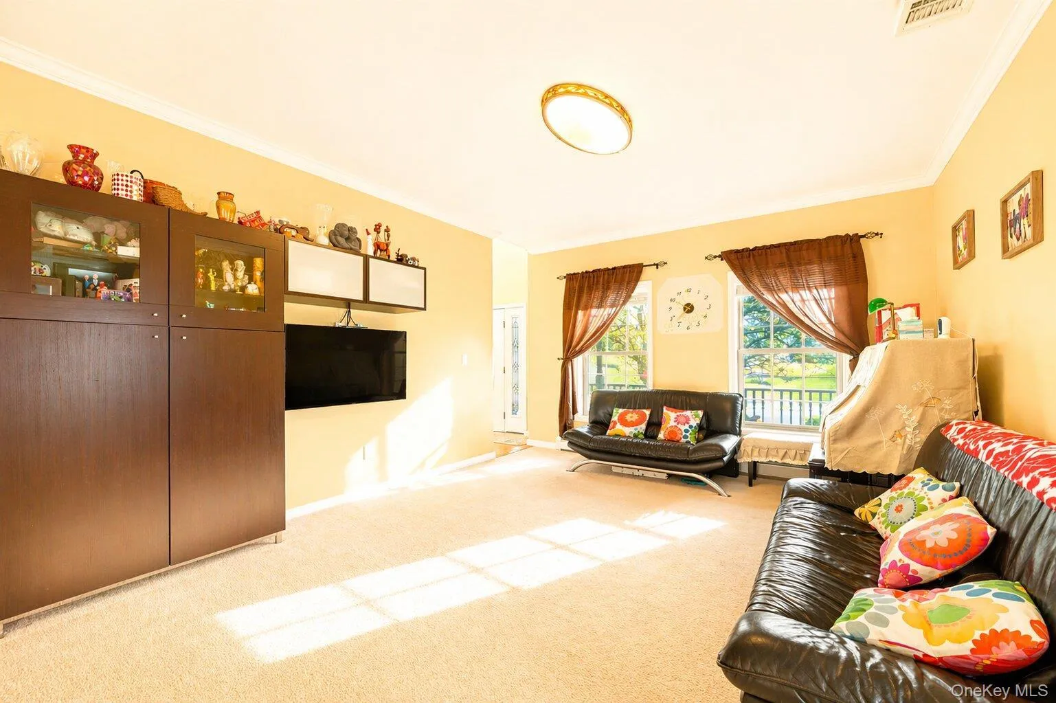 Spacious living area featuring neutral carpeting, light-toned wall paint, and crown molding Spacious living area featuring neutral carpeting, light-toned wall paint, and crown molding