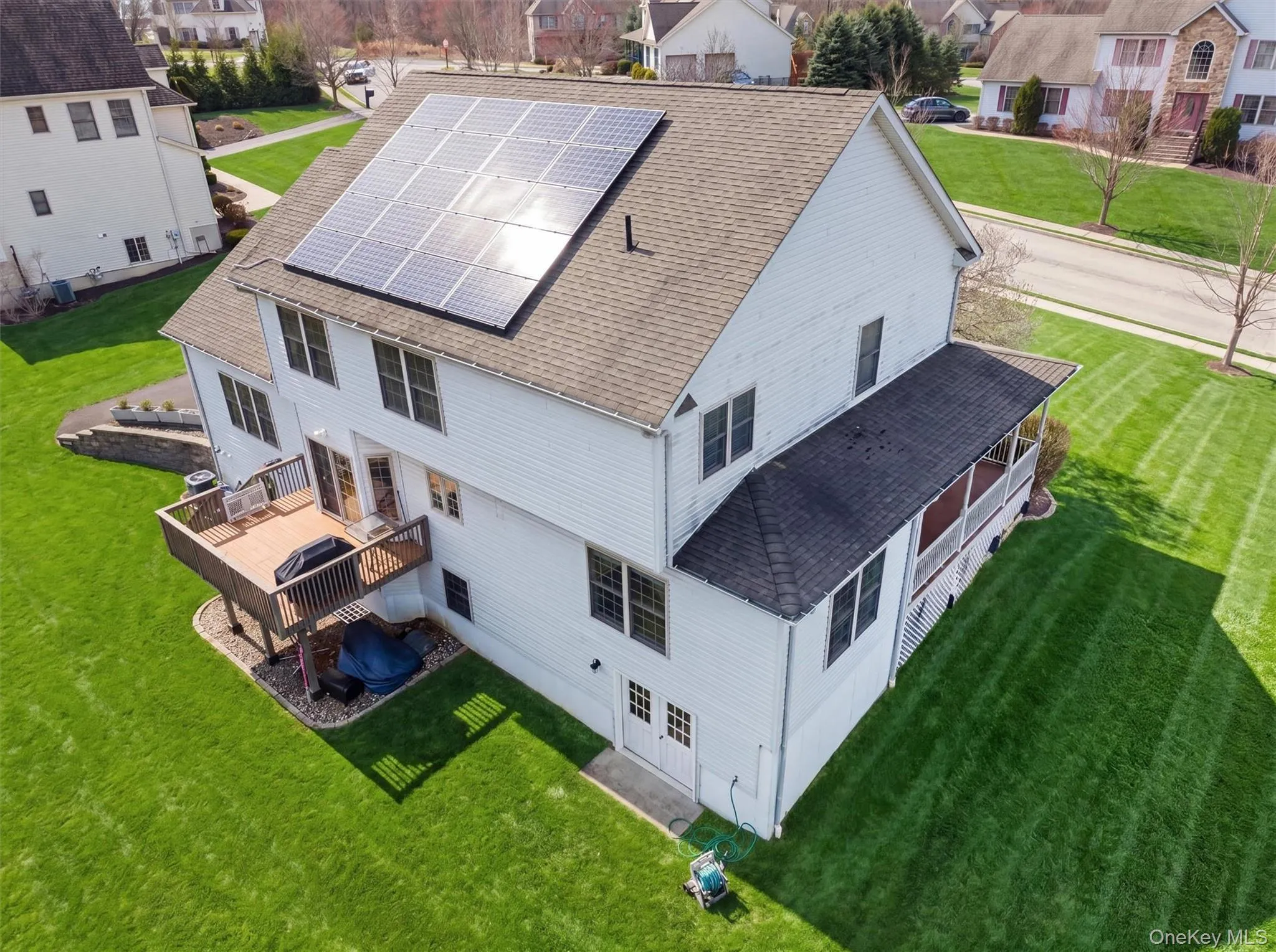 White two-story residence featuring solar panels, a multi-paneled deck with railing, and an attached screened porch White two-story residence featuring solar panels, a multi-paneled deck with railing, and an attached screened porch