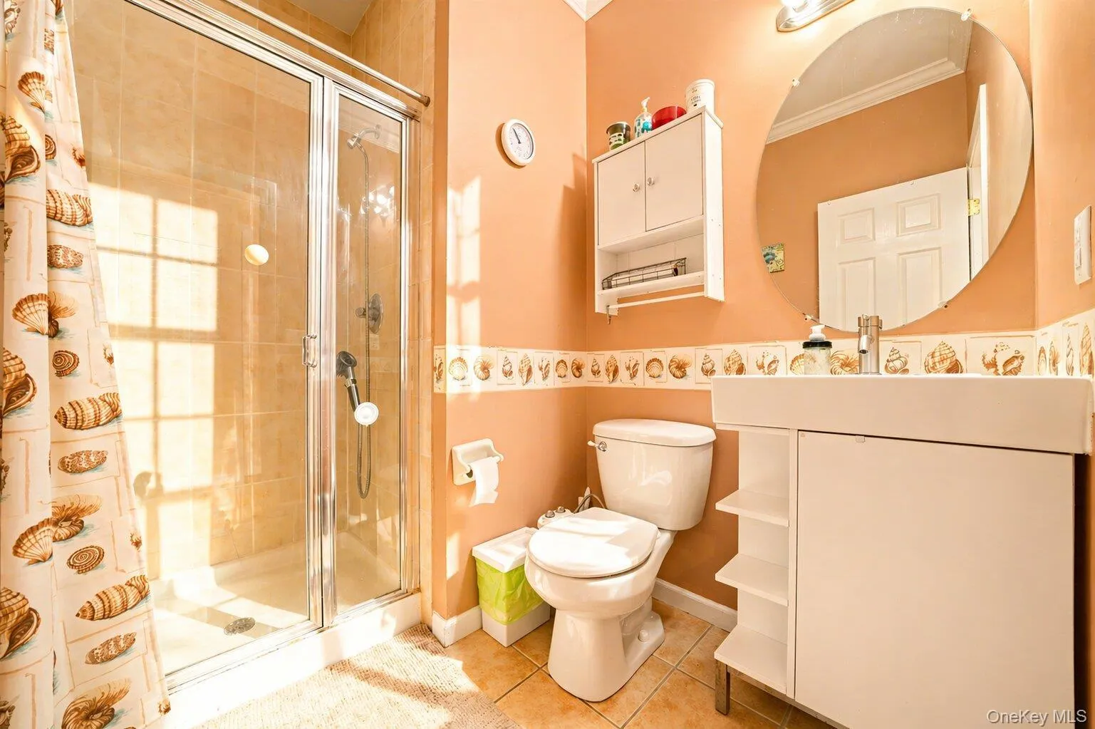 Full bathroom featuring a glass-enclosed shower with tiled walls, a white vanity with integrated basin, an oval wall-mounted mirror, and a built-in wall cabinet with open shelving Full bathroom featuring a glass-enclosed shower with tiled walls, a white vanity with integrated basin, an oval wall-mounted mirror, and a built-in wall cabinet with open shelving