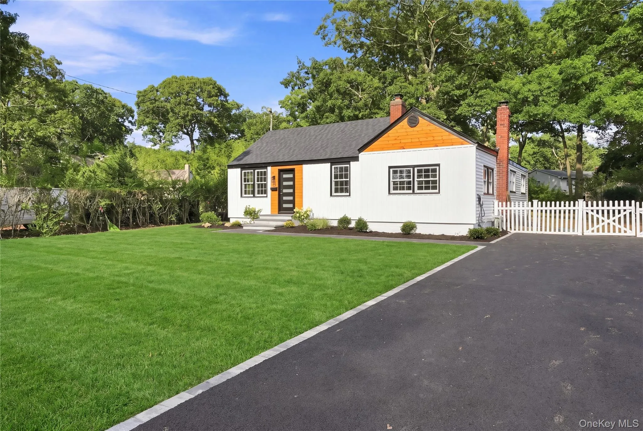 White siding exterior with a dark shingle roof, wood shake accent siding, a brick chimney, and a black front door with vertical window panels White siding exterior with a dark shingle roof, wood shake accent siding, a brick chimney, and a black front door with vertical window panels