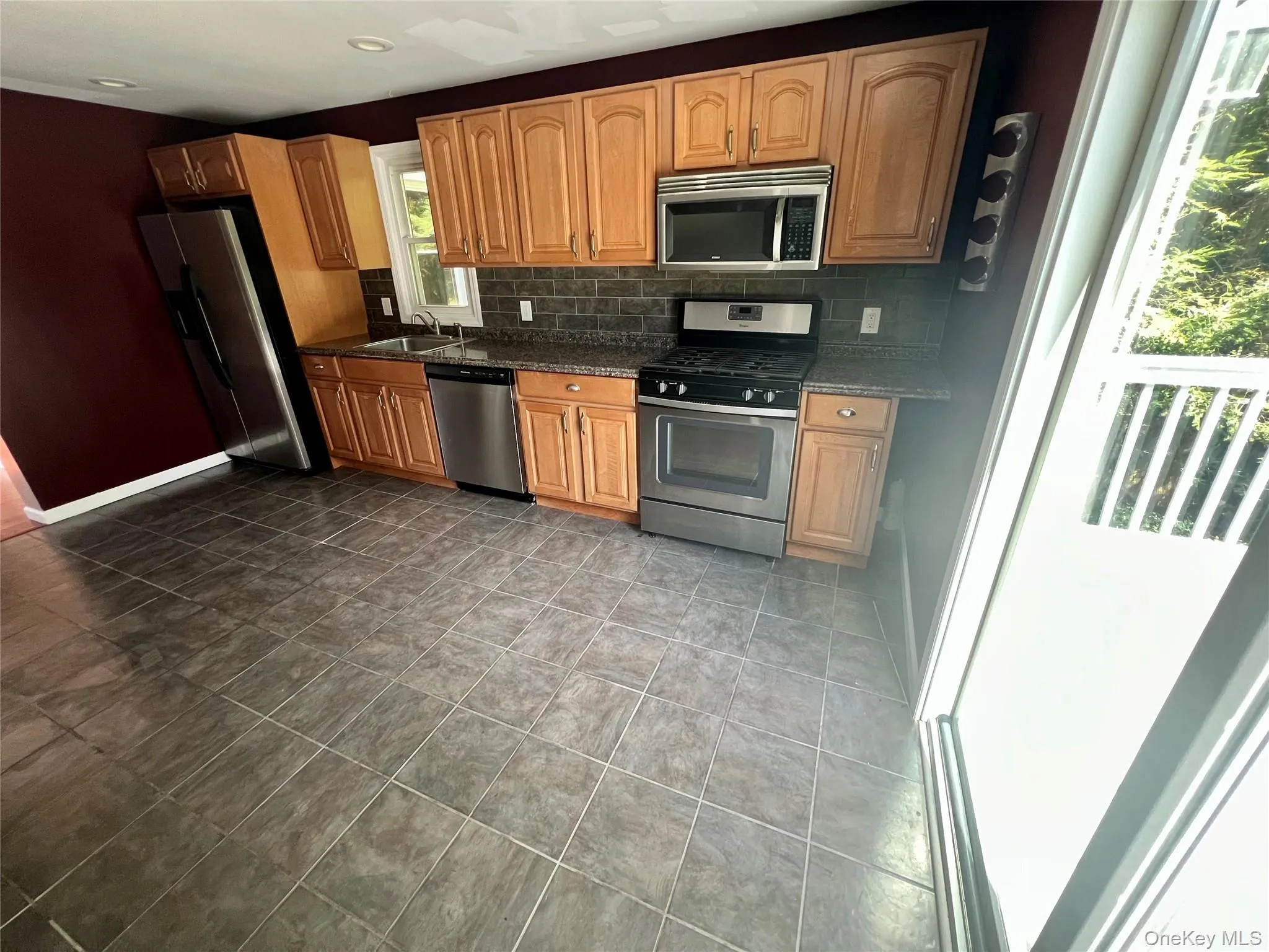 Kitchen featuring stainless steel appliances, wood cabinetry, stone countertops, and tile flooring Kitchen featuring stainless steel appliances, wood cabinetry, stone countertops, and tile flooring