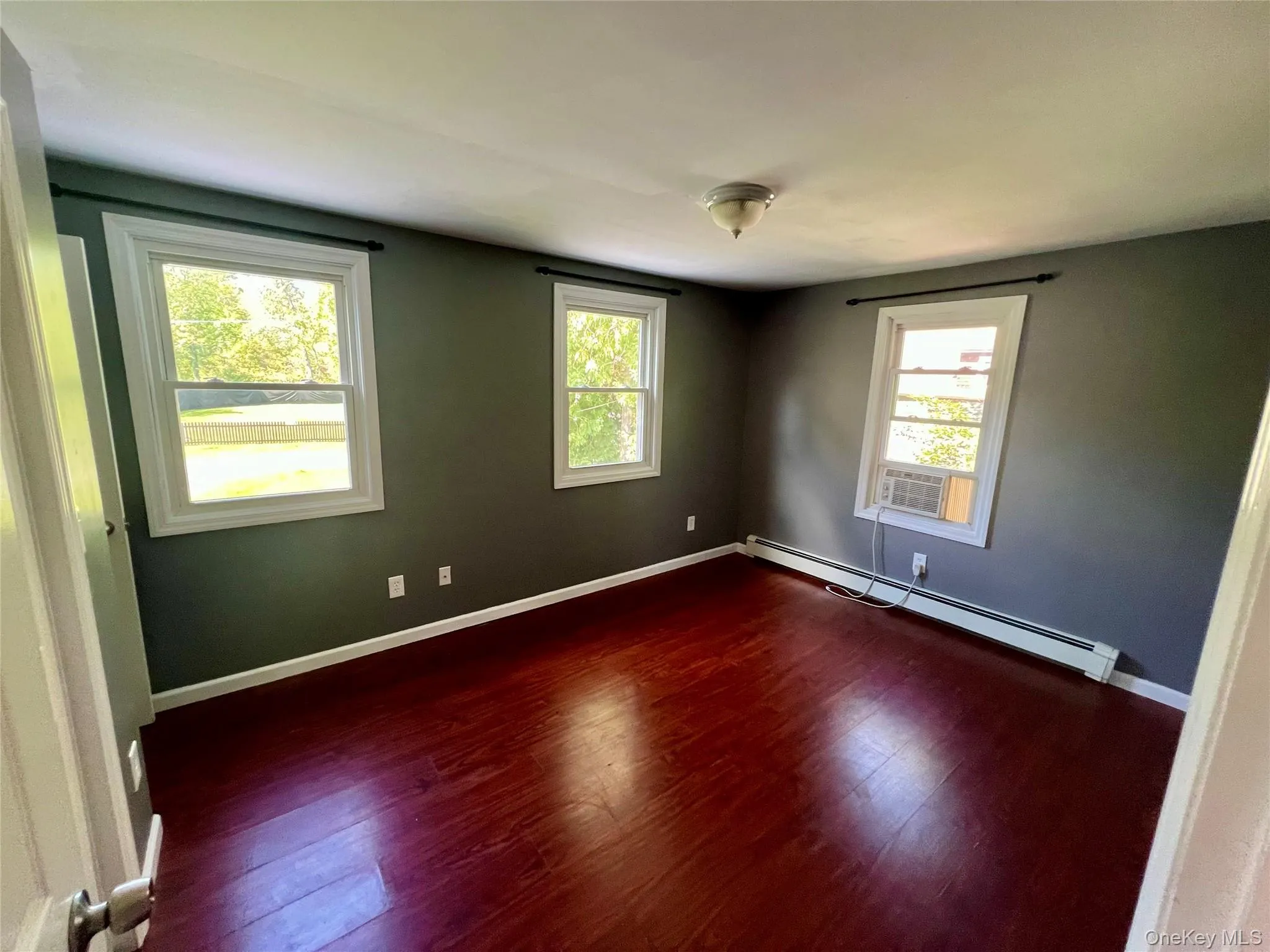 Rich wood-finish flooring, multiple windows with white trim, and a ceiling-mounted light fixture Rich wood-finish flooring, multiple windows with white trim, and a ceiling-mounted light fixture