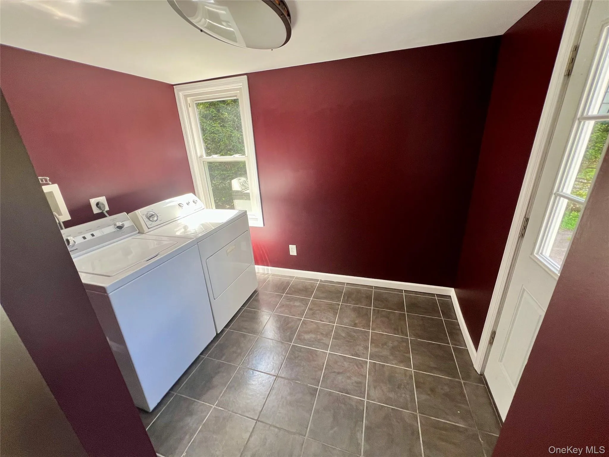 Laundry area featuring tile flooring, a window, and a white door Laundry area featuring tile flooring, a window, and a white door