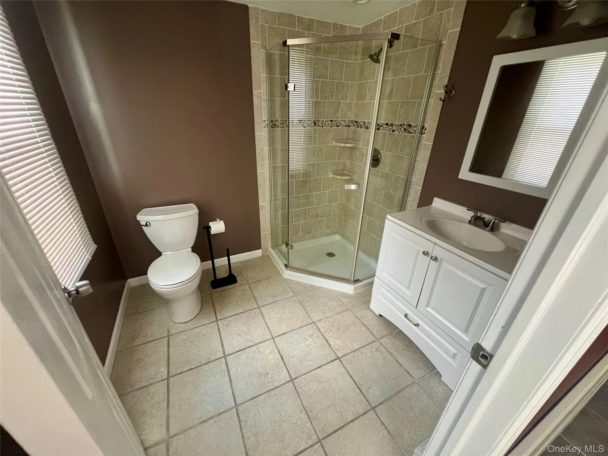 Tiled flooring with a corner glass-enclosed shower, featuring a decorative accent band Tiled flooring with a corner glass-enclosed shower, featuring a decorative accent band