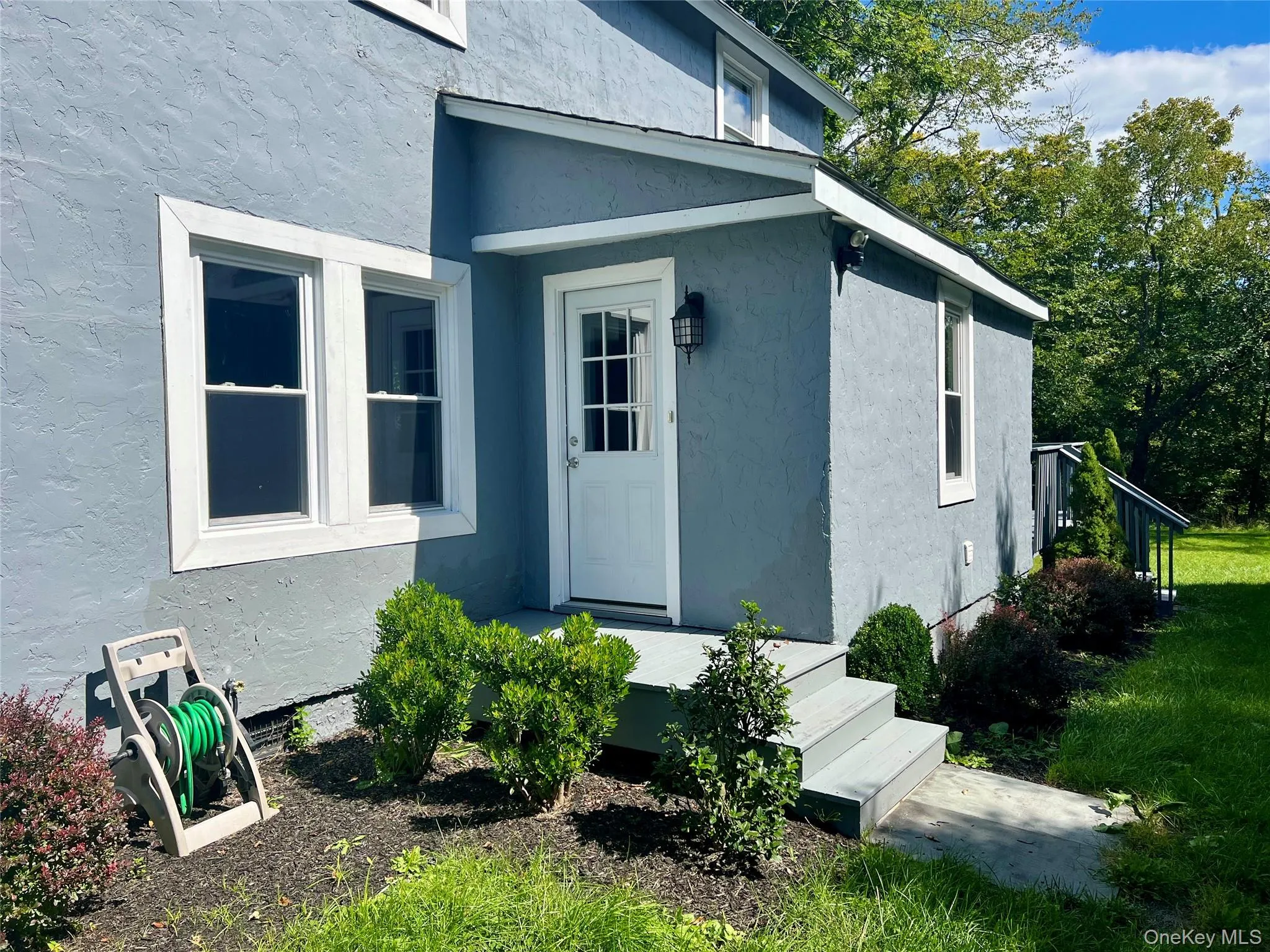 Stucco exterior with white trim, featuring a white paneled door with glass inserts, an exterior wall lantern, and a raised entryway with steps Stucco exterior with white trim, featuring a white paneled door with glass inserts, an exterior wall lantern, and a raised entryway with steps