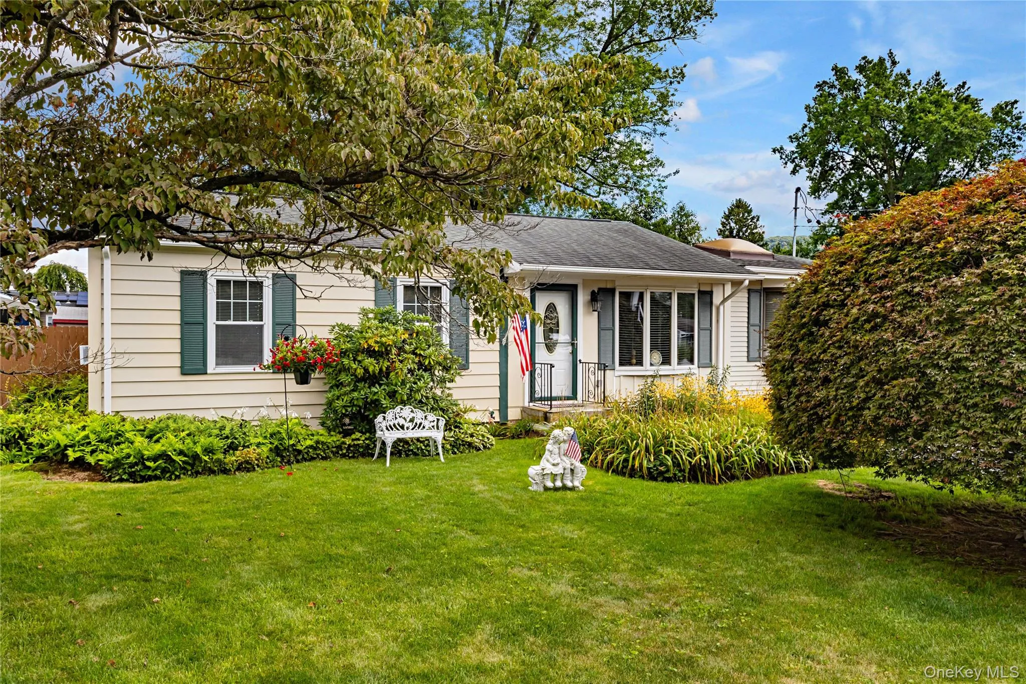 Single-story residence featuring light-colored siding, multiple windows with green shutters, a front entry with a storm door, and a bay window Single-story residence featuring light-colored siding, multiple windows with green shutters, a front entry with a storm door, and a bay window