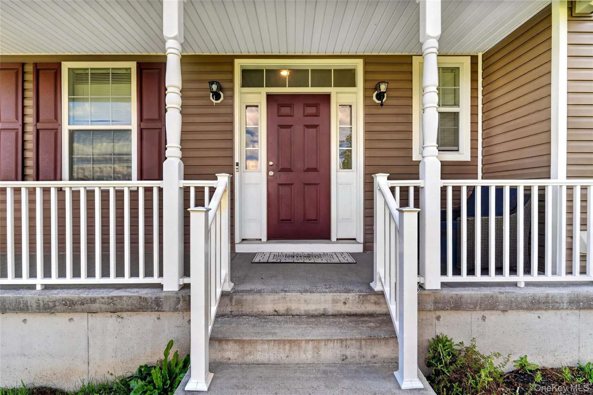 Covered front porch with white railings, a rich red entry door, and two exterior wall sconces Covered front porch with white railings, a rich red entry door, and two exterior wall sconces