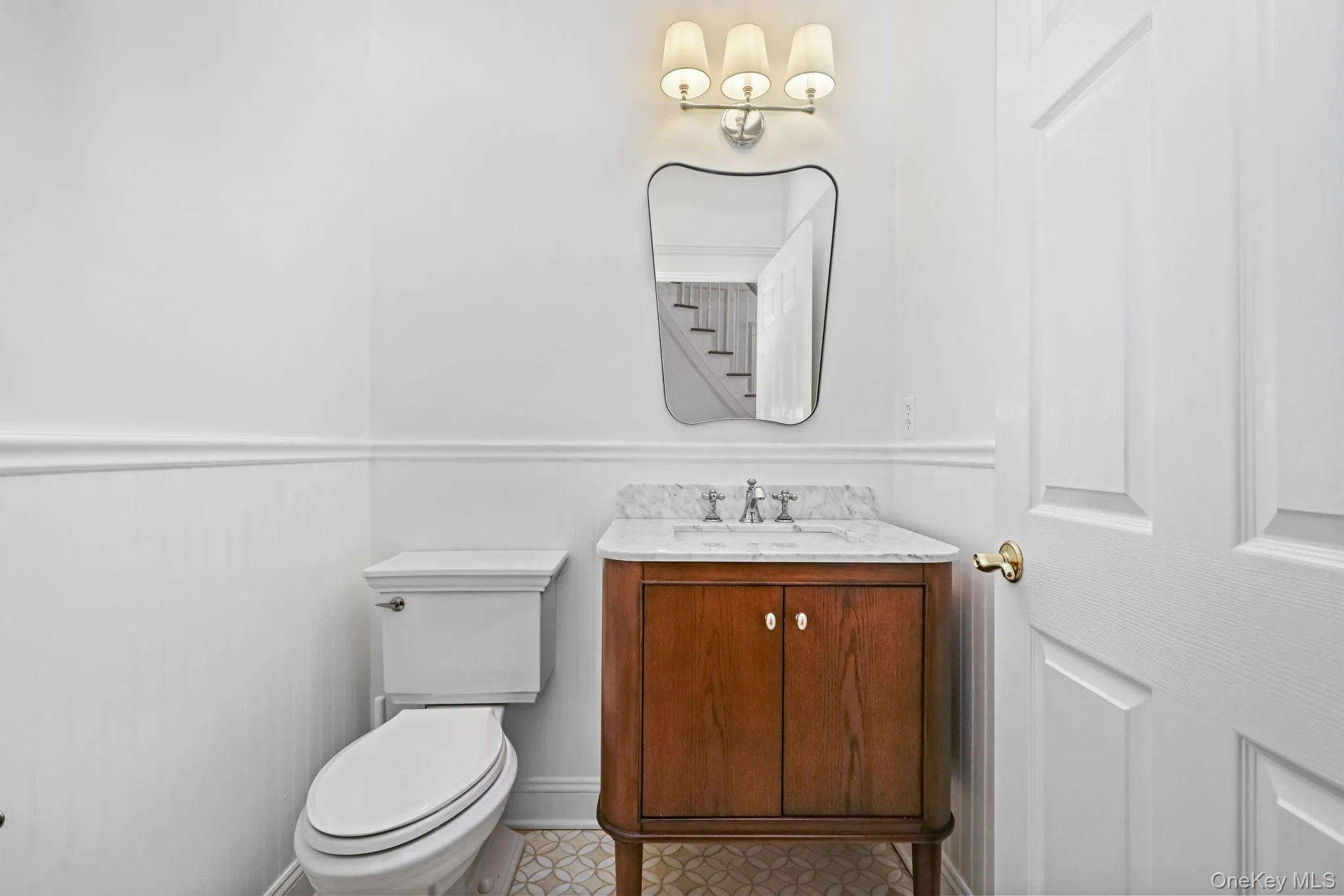 An oak vanity with Carrara marble top, marble and limestone flooring and wainscoting adorn the powder room. An oak vanity with Carrara marble top, marble and limestone flooring and wainscoting adorn the powder room.
