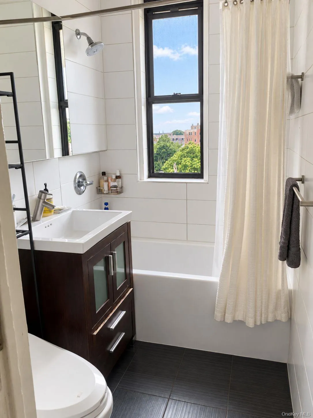 Bathroom featuring a dark wood-finish vanity with a white vessel sink, a white bathtub, dark tile flooring, and white subway tile walls Bathroom featuring a dark wood-finish vanity with a white vessel sink, a white bathtub, dark tile flooring, and white subway tile walls