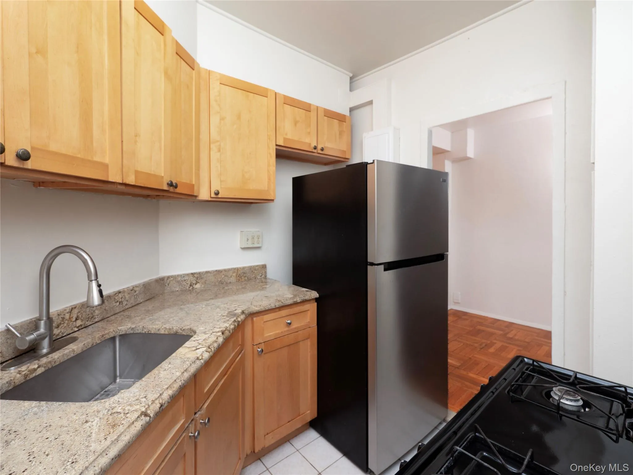 Stainless steel refrigerator, light wood-finish cabinetry, speckled countertop, stainless steel sink with gooseneck faucet, and gas range Stainless steel refrigerator, light wood-finish cabinetry, speckled countertop, stainless steel sink with gooseneck faucet, and gas range